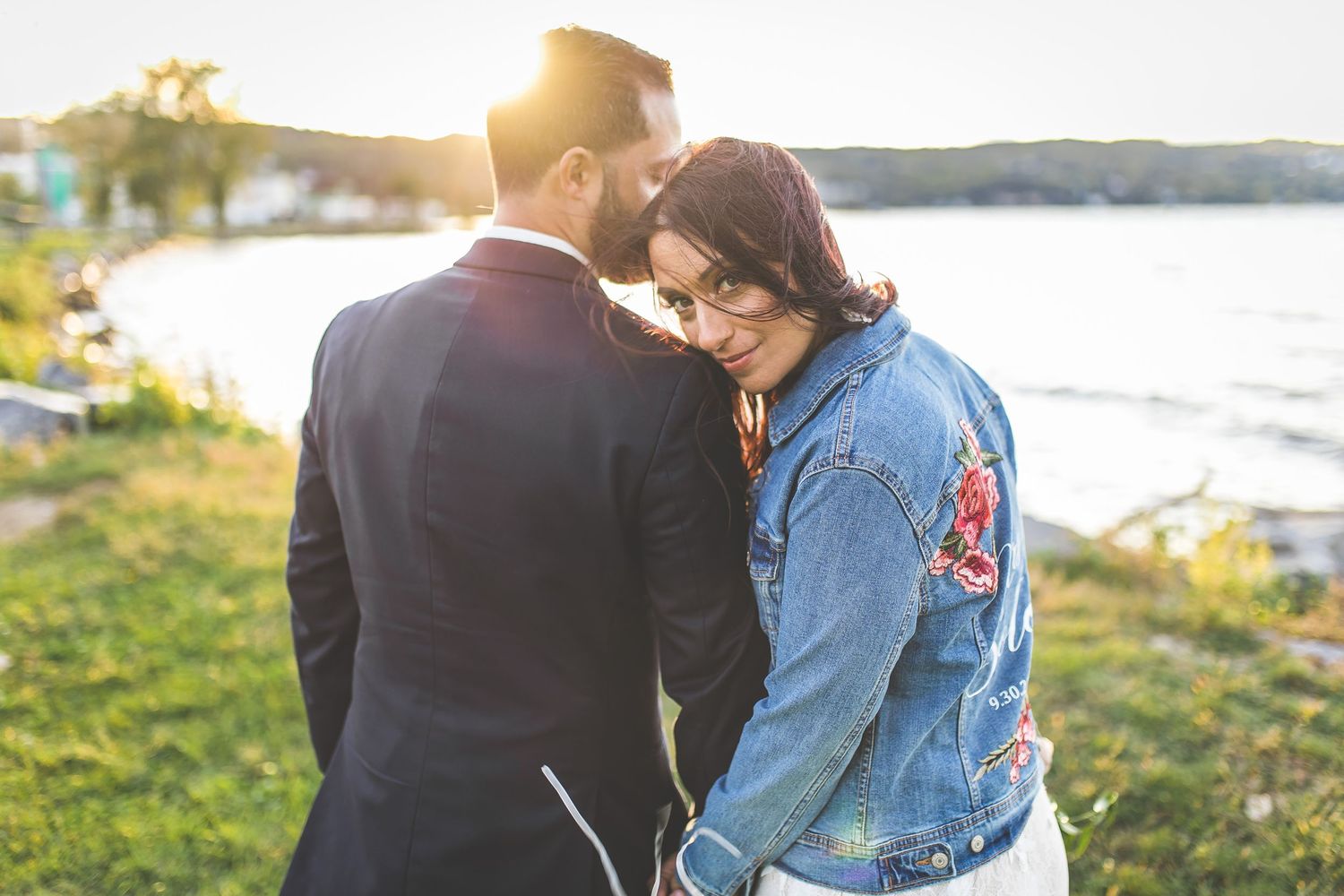 Wedding couple strolls along grassy waterfront path at sunset.