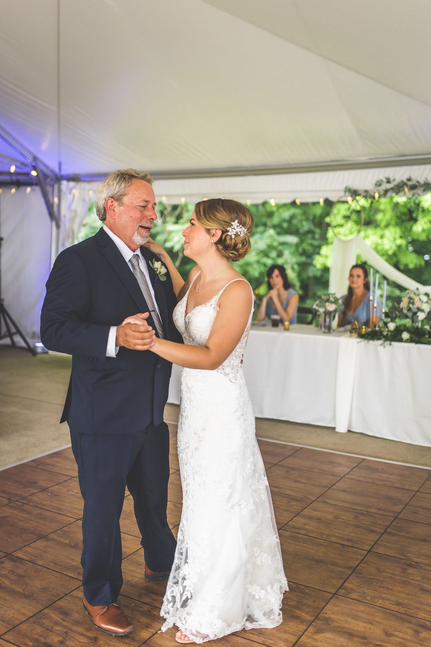 A tender father-daughter dance at a wedding reception under a white tent with wooden flooring.