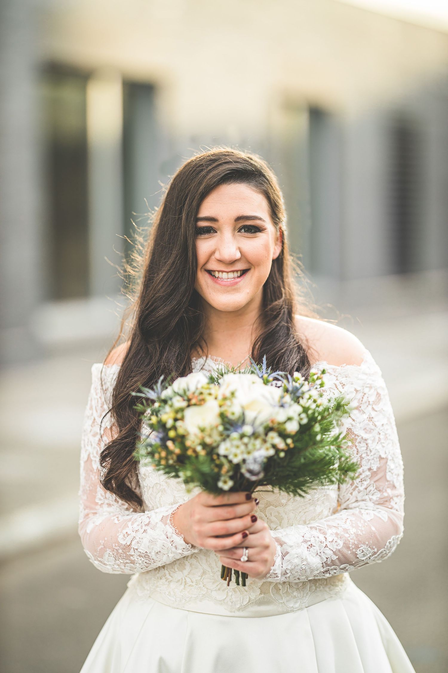 Joyful bridal portrait with white floral bouquet against neutral background.