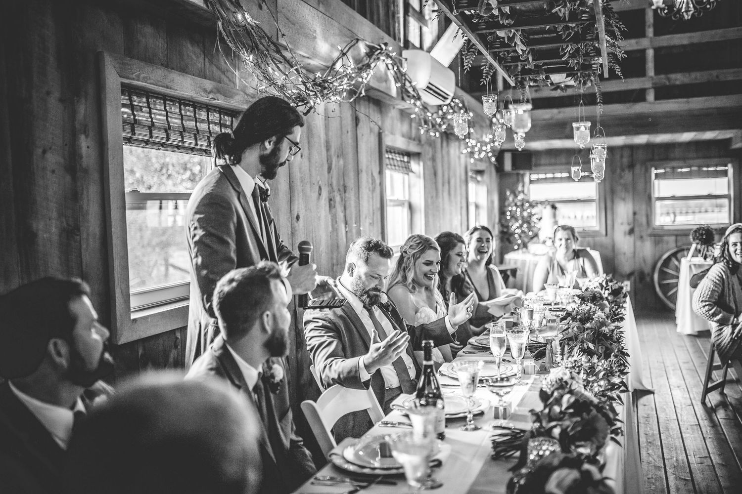 Wedding reception candid moments captured in black and white at rustic venue.