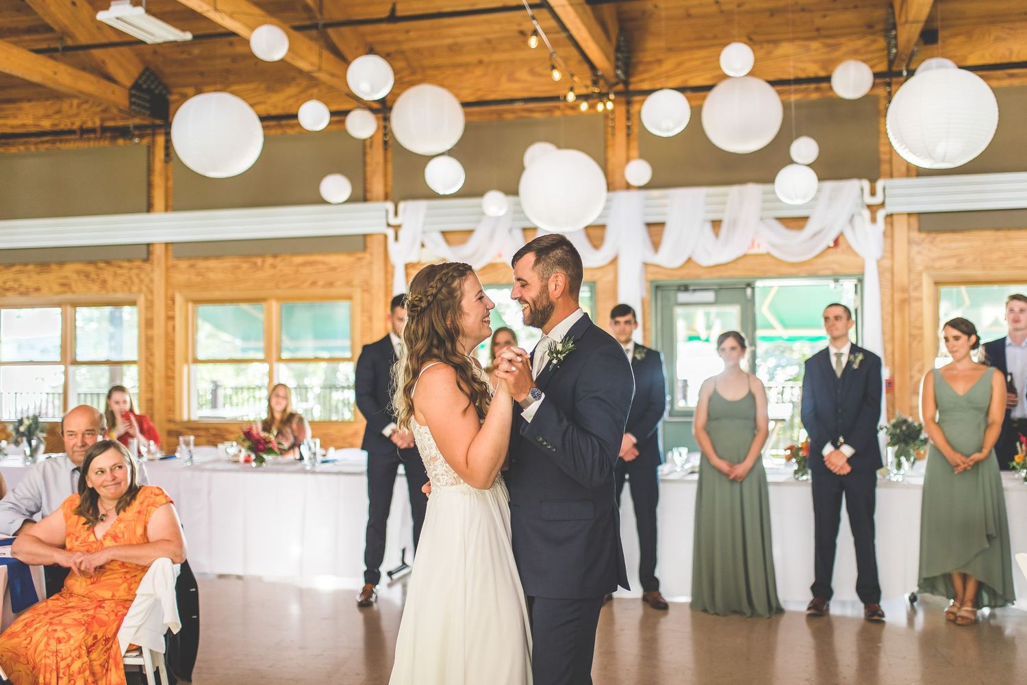 Wedding reception venue features romantic white drapery and paper lanterns hanging from wooden rafters.