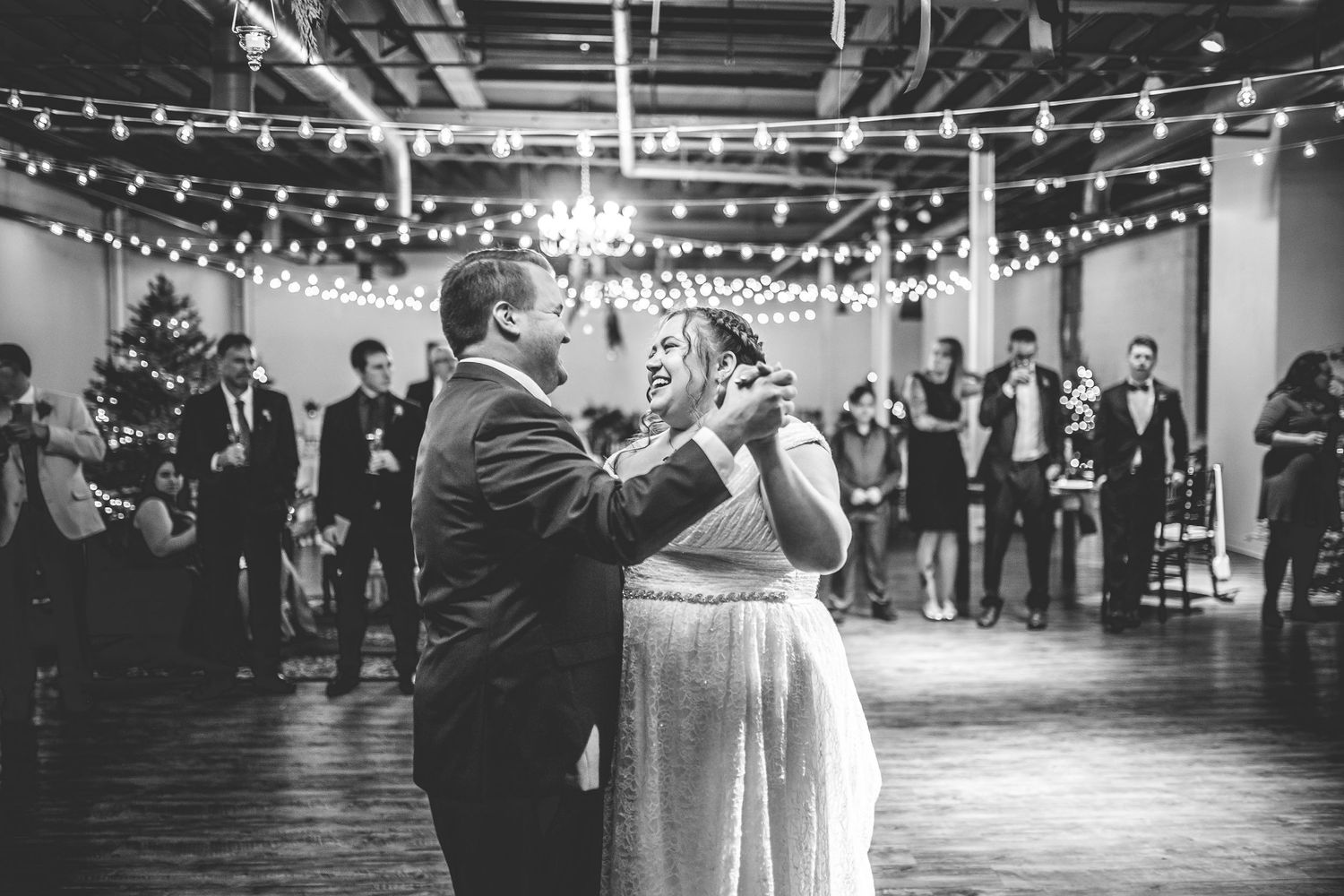 Couples dance together at a wedding reception under string lights and chandeliers.