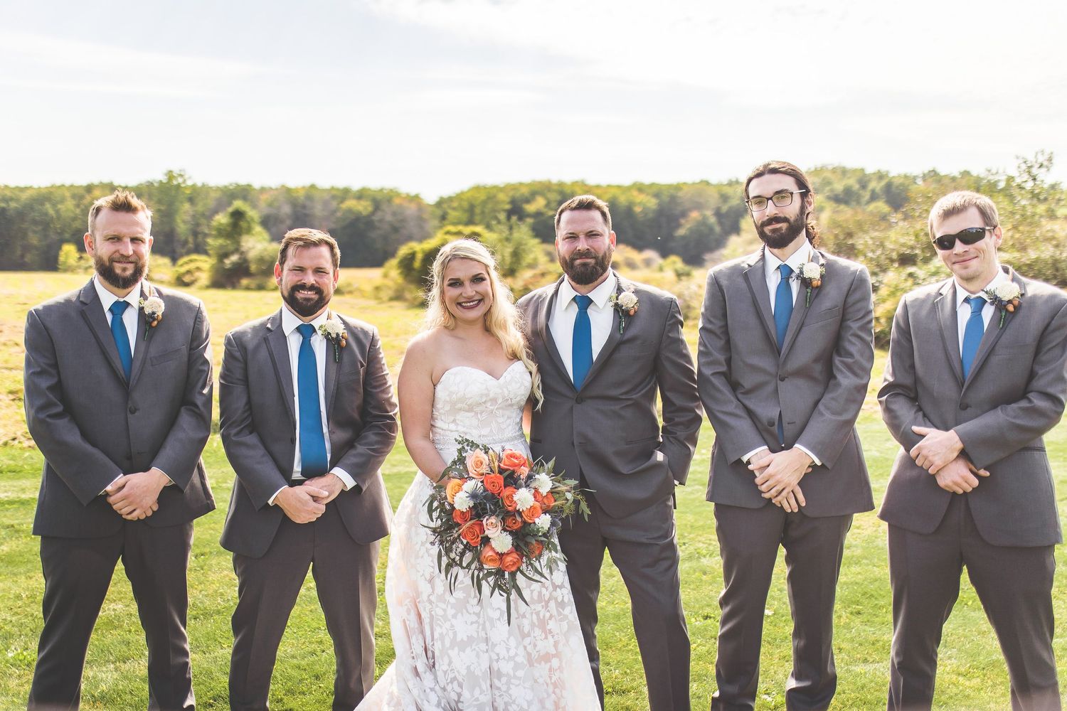 Wedding party in navy blue dresses and gray suits poses together on a sunny hillside.