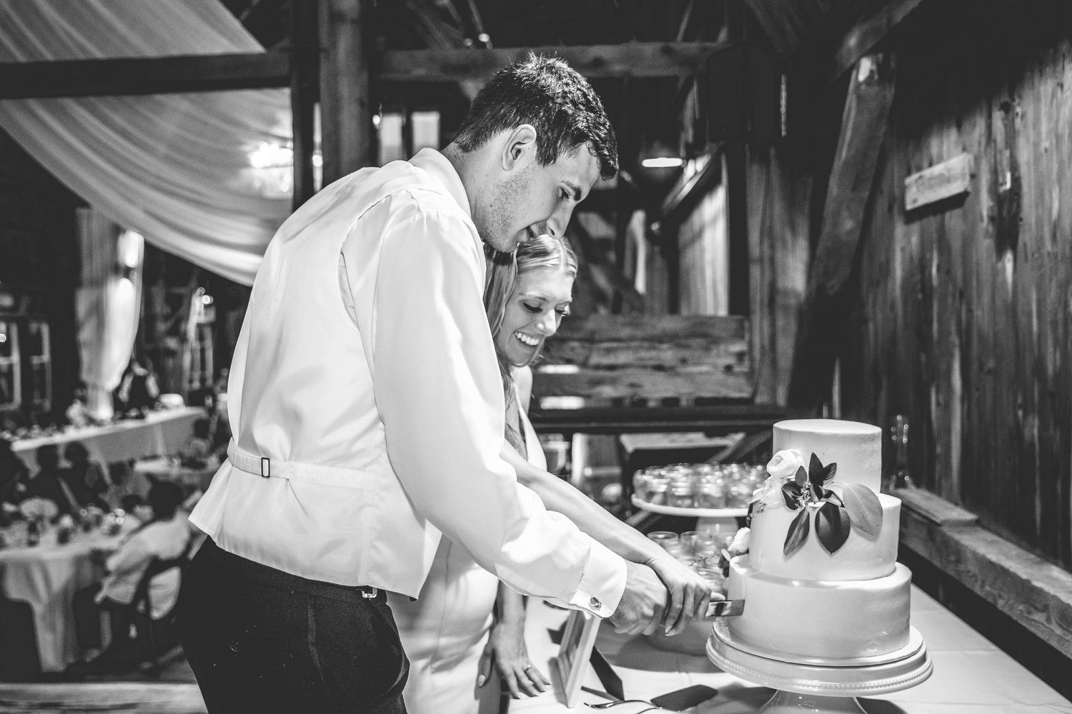 A couple cuts their elegant white wedding cake together at their reception celebration.