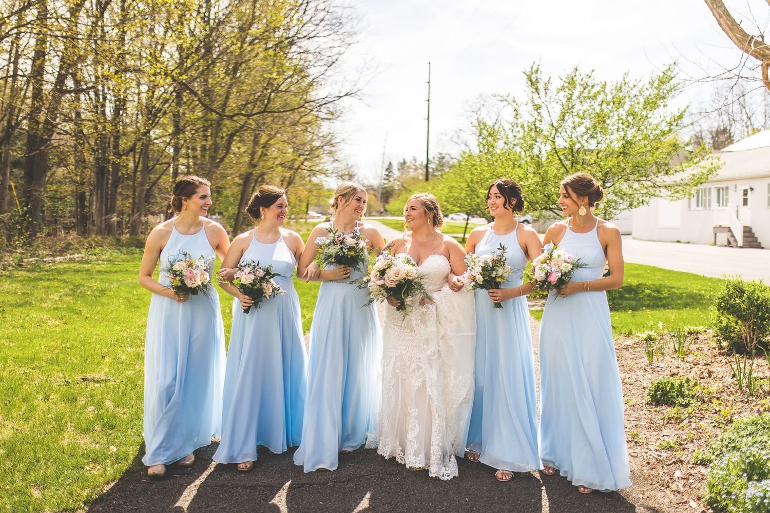 Bridal party in powder blue dresses poses together on a sunny spring day.