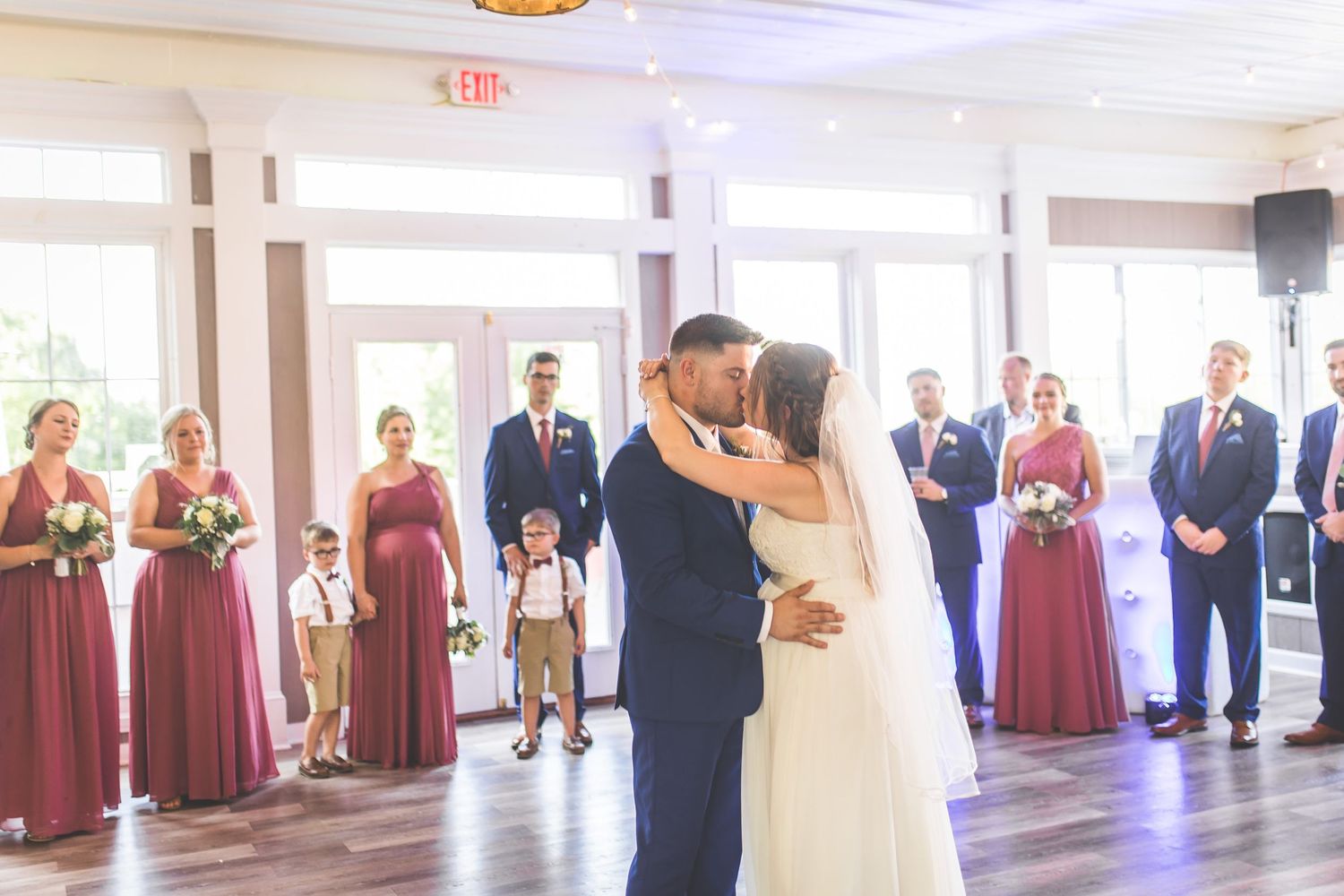 Wedding reception hall decorated with chandeliers and burgundy accents as couple dances.