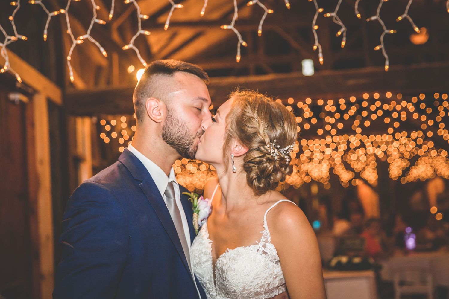 Romantic wedding reception moment under warm string lights in rustic barn setting.