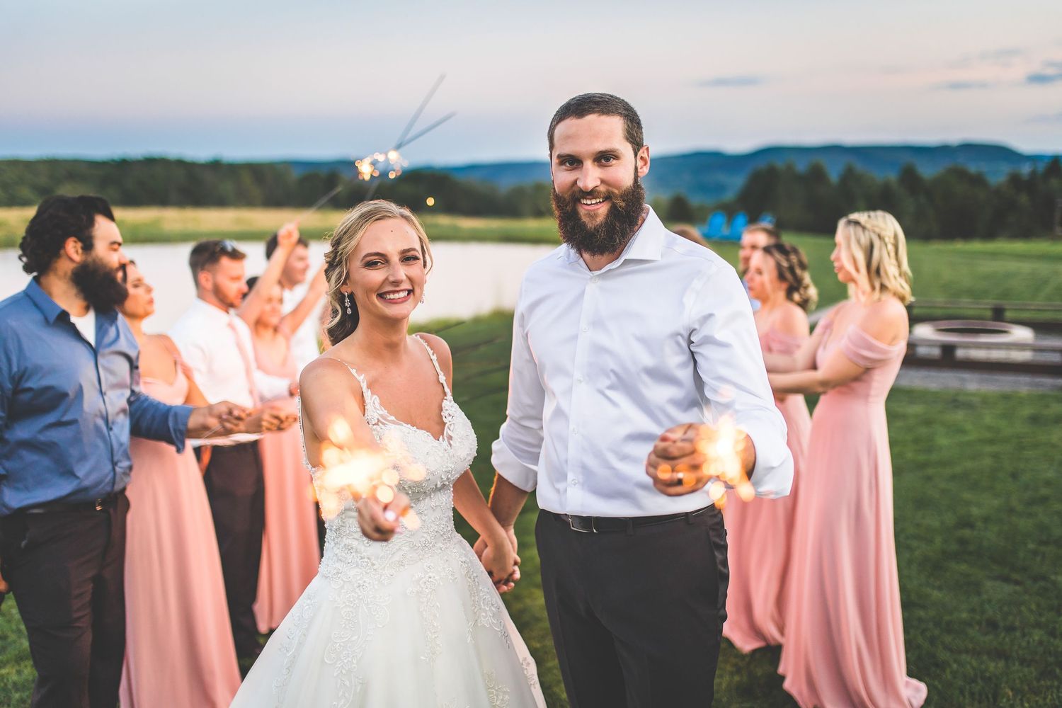 Wedding party forming sparkler tunnel against mountain backdrop at sunset.