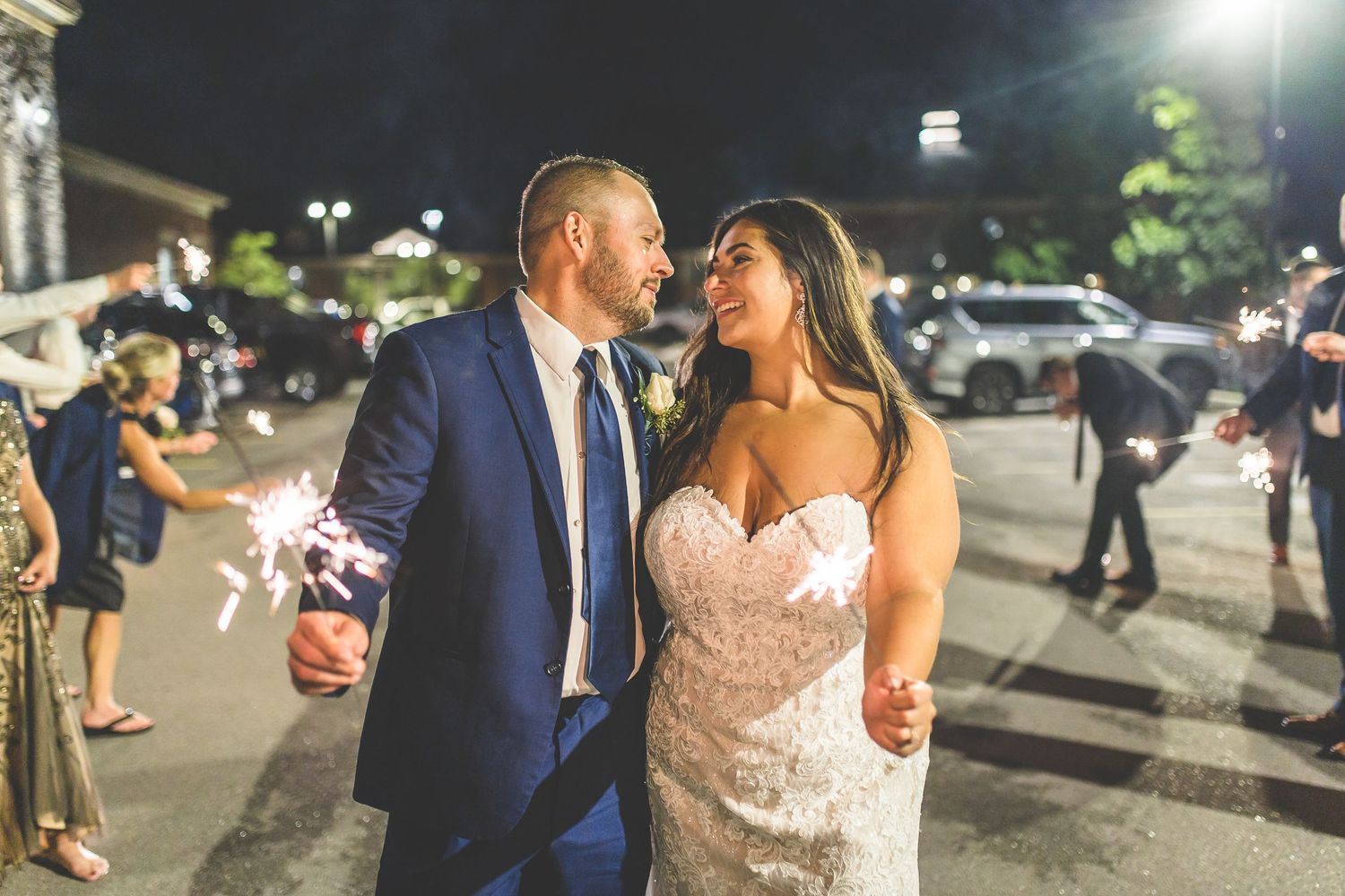 Couple celebrating their wedding exit through sparkler tunnel at night.