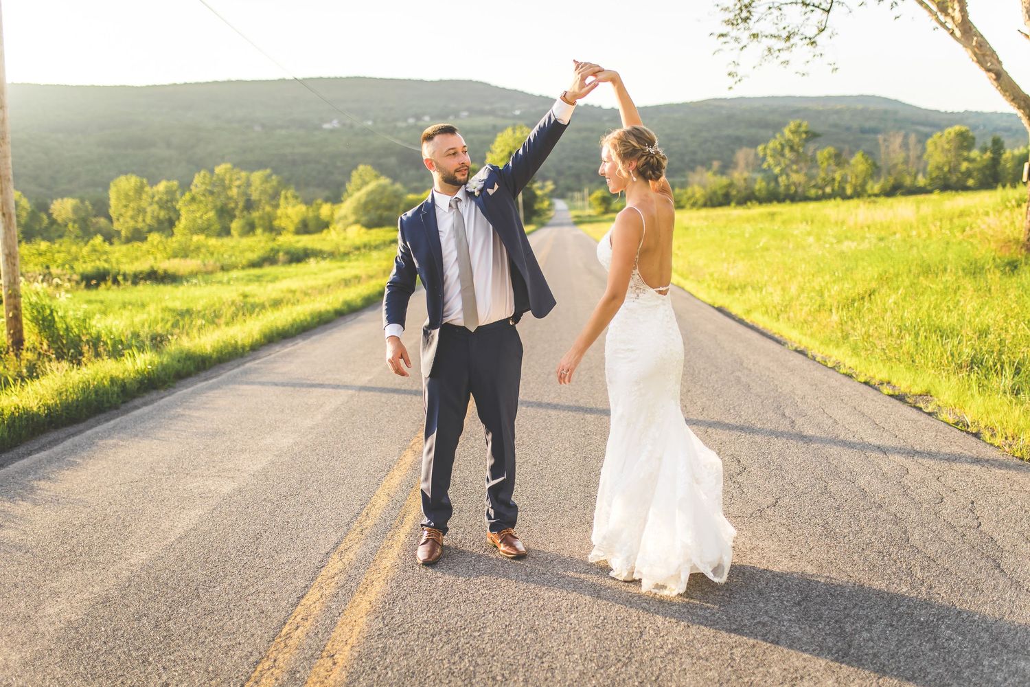 Newlyweds walking and dancing on a country road at sunset.