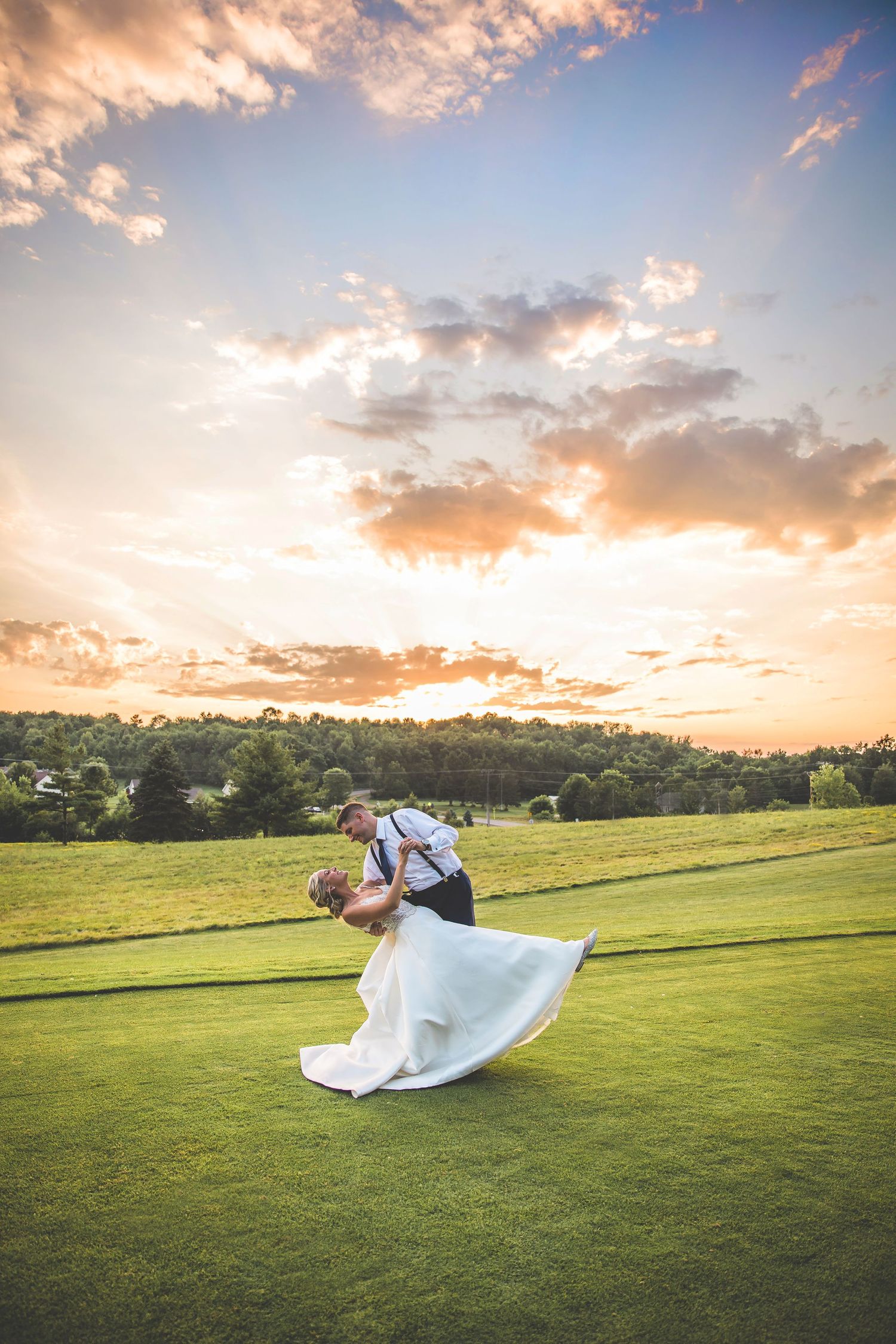 Dramatic sunset wedding photo with couple in romantic dip pose on golf course.