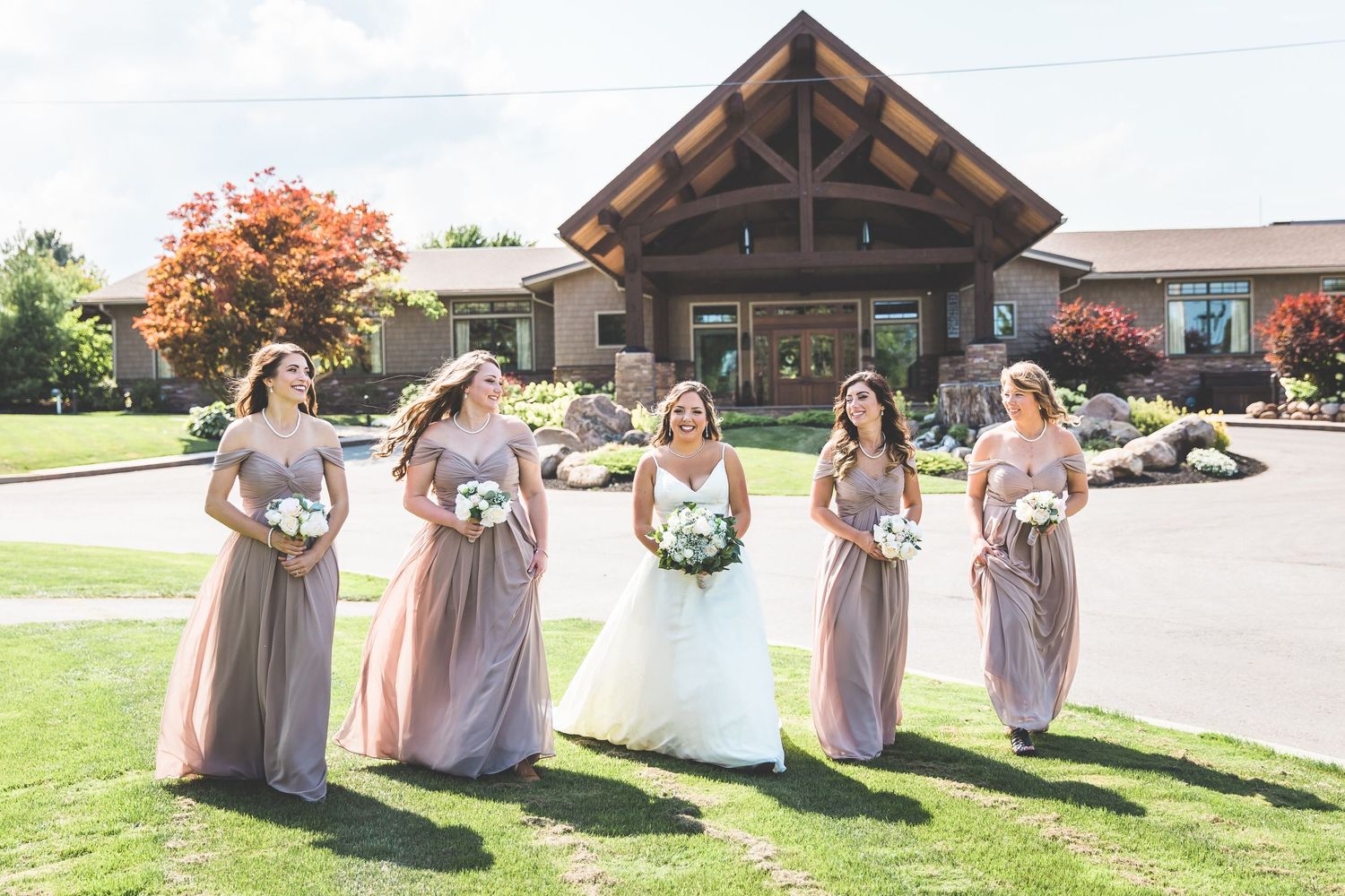 Bridesmaids in blush dresses pose together outdoors on a sunny wedding day.