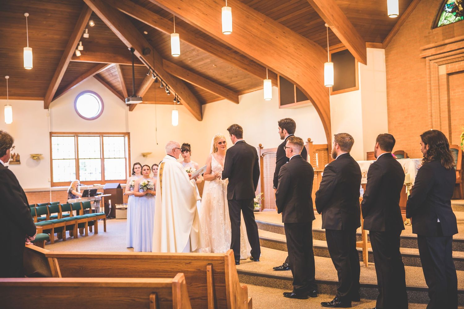 Wedding ceremony in a church with wooden beams and pendant lighting.