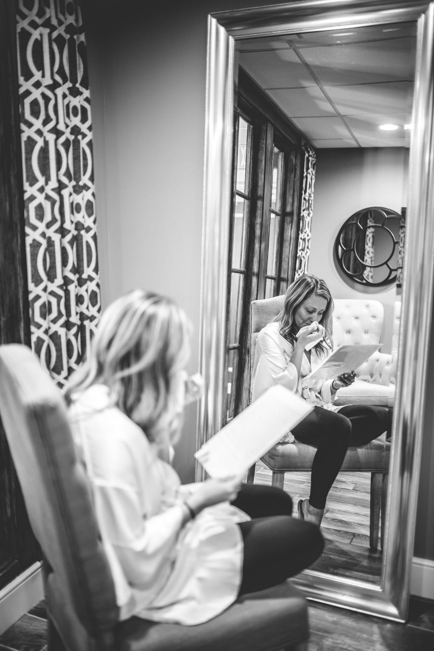 Black and white photo of preparation moments in elegant room with decorative mirrors.