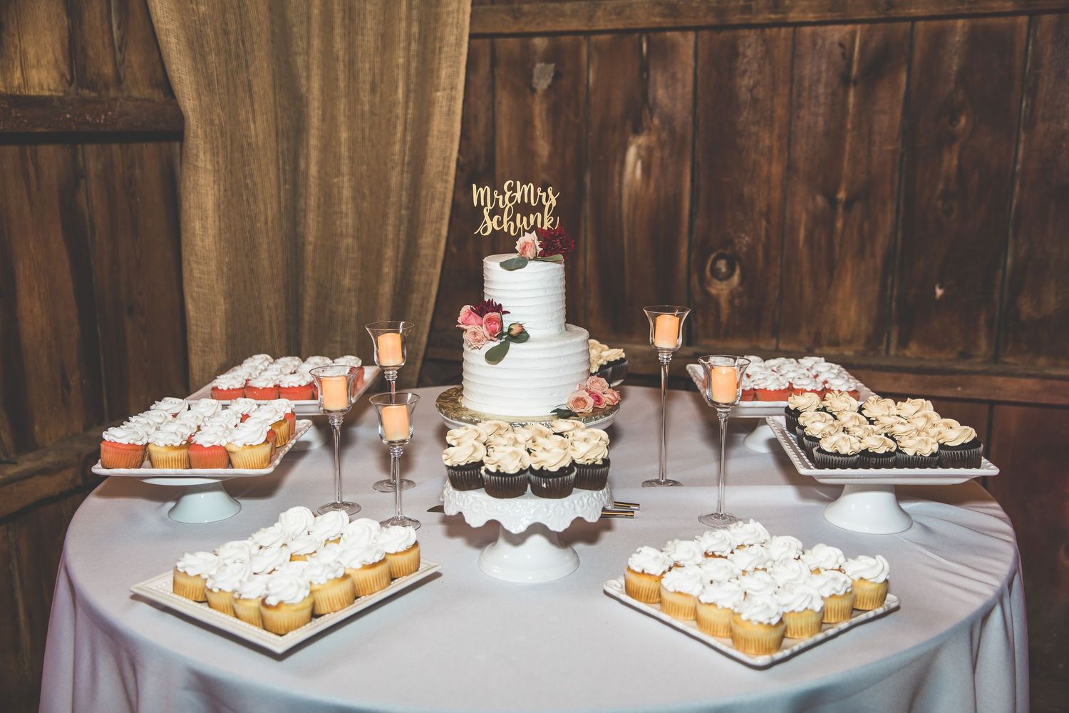Elegant white wedding cake and dessert display on rustic wooden table setting.