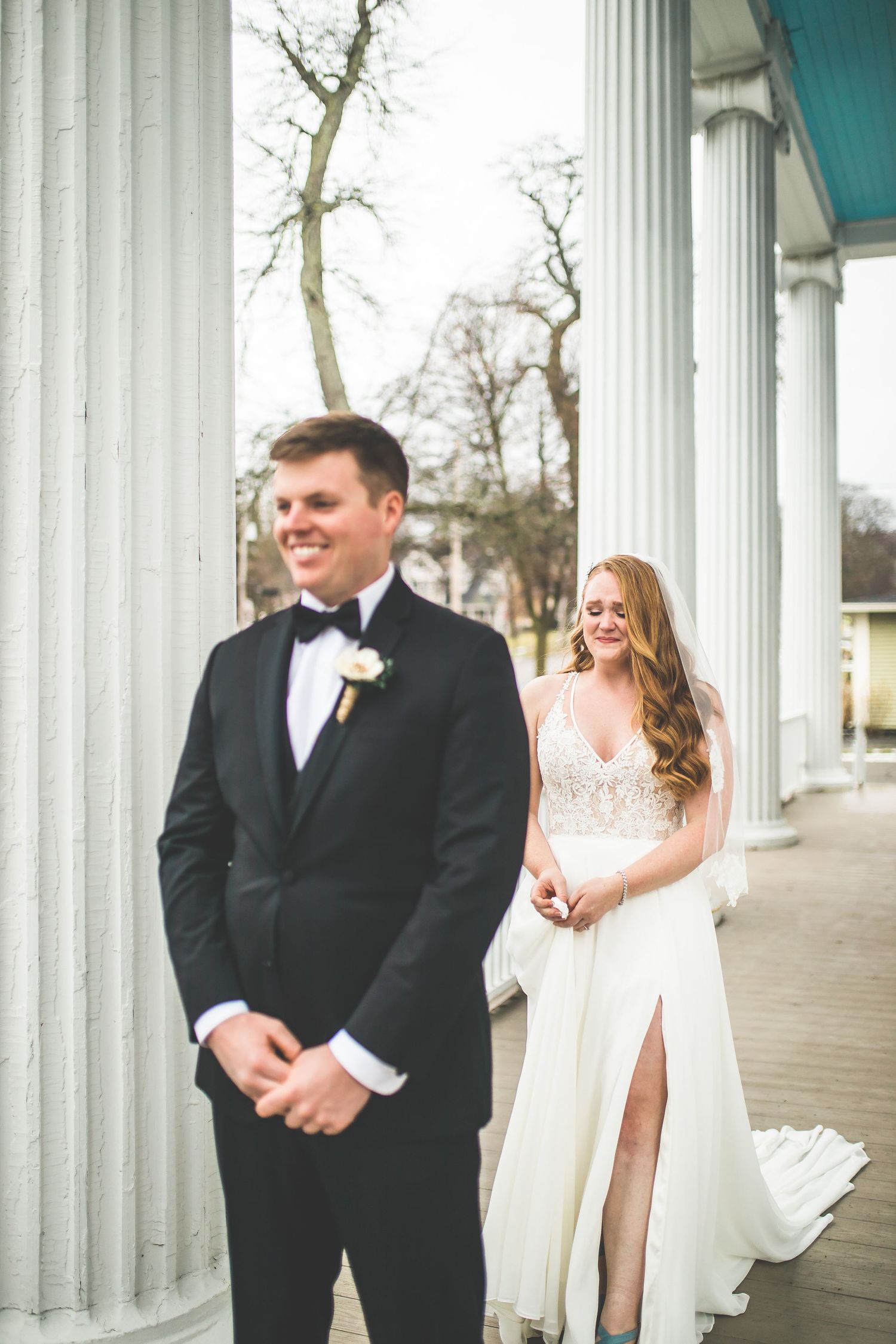 A joyful wedding couple sharing a moment among white columns on a covered porch.