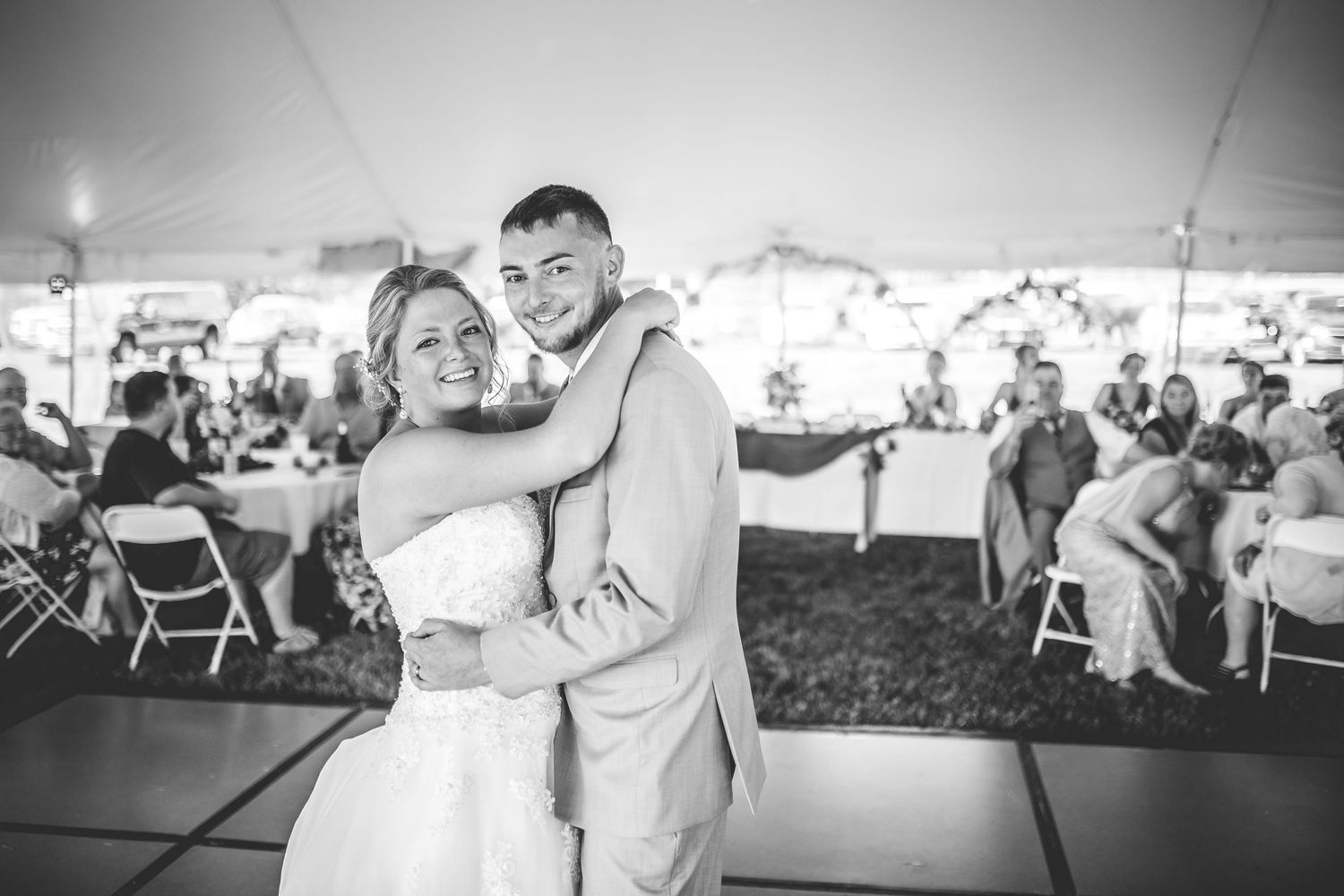 Happy couple dances and laughs together during their wedding reception under a tent.