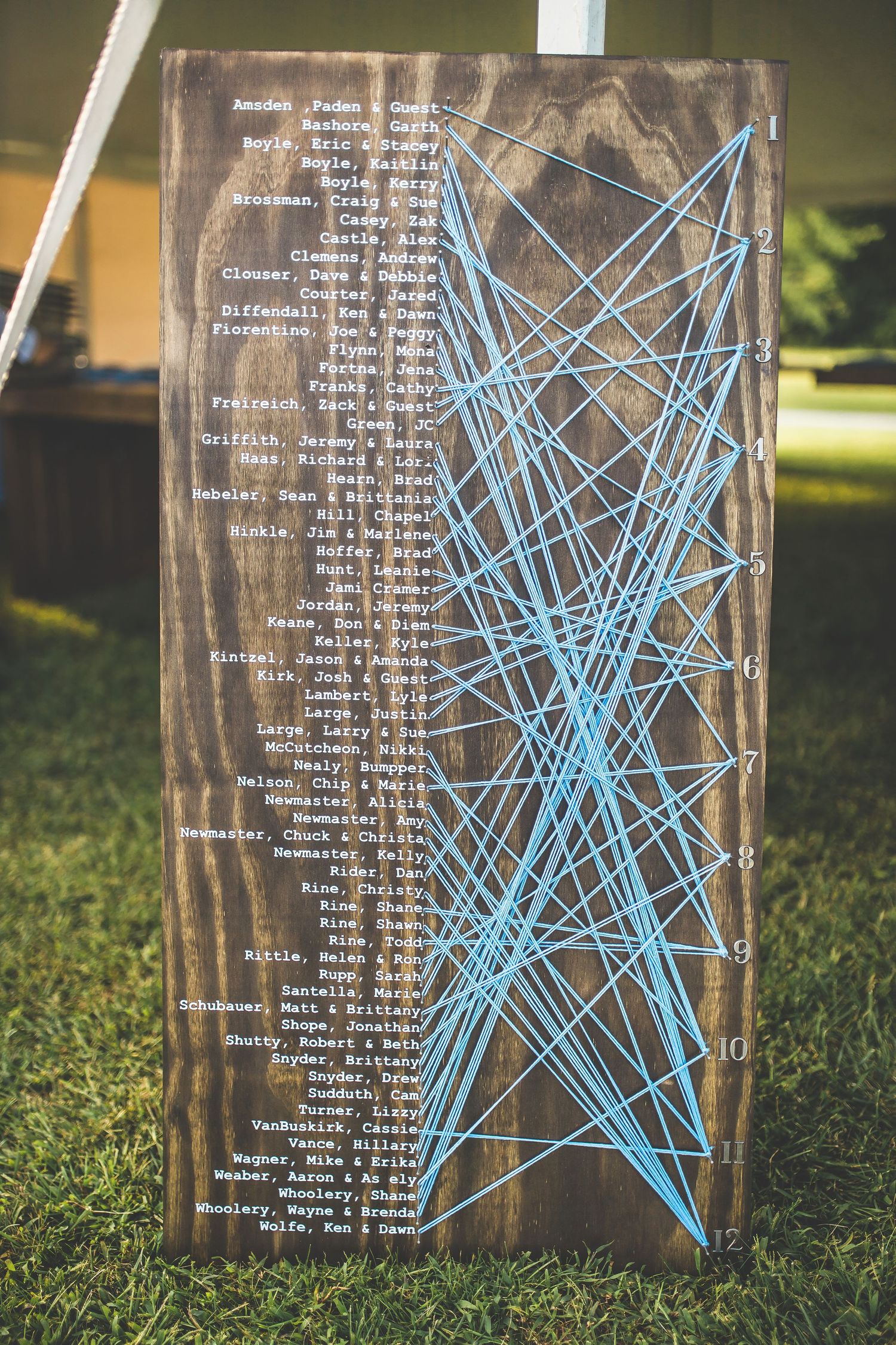 Rustic wooden seating chart with blue string art star design displays wedding guest names.