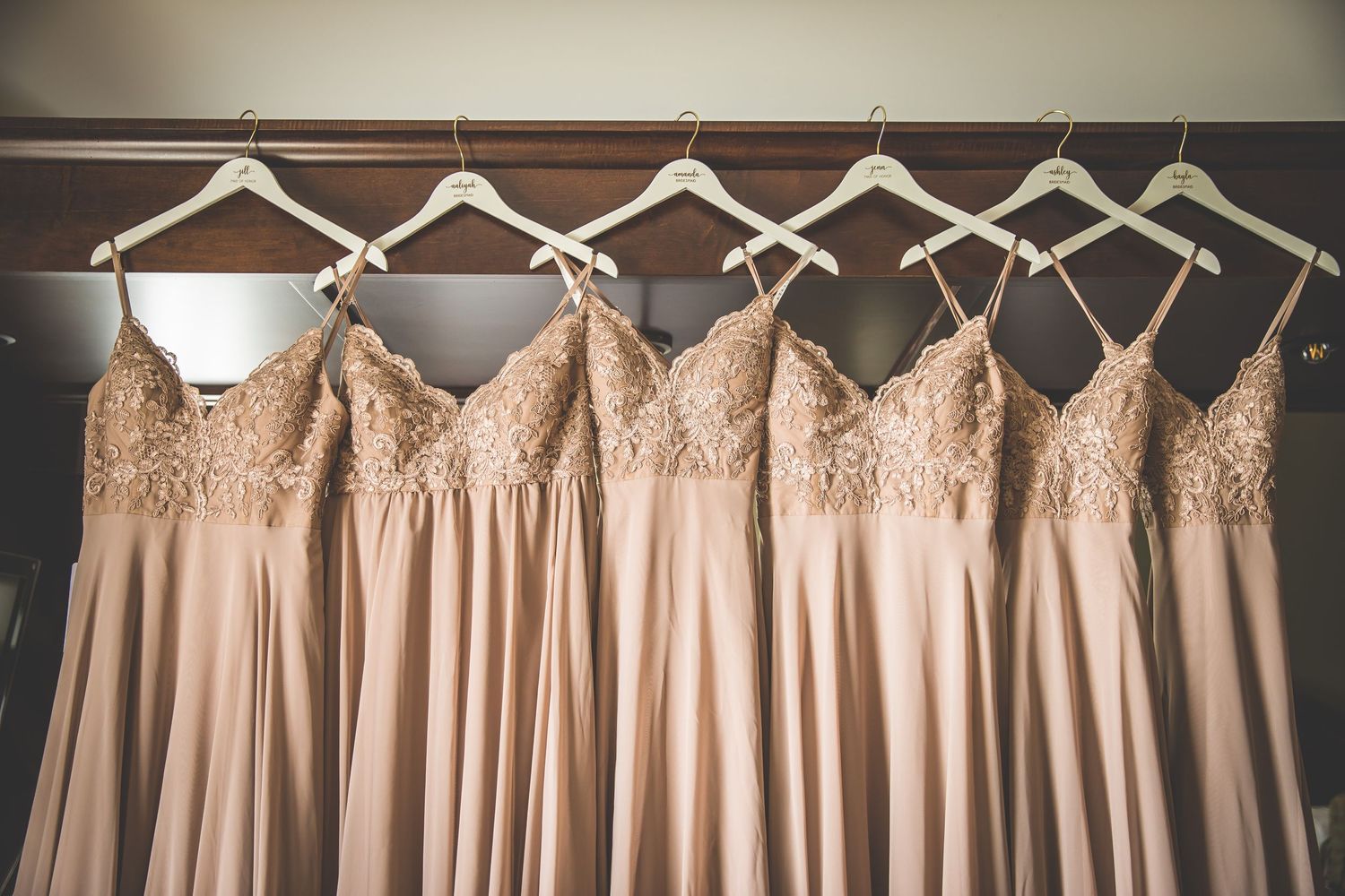 Row of blush pink bridesmaid dresses hanging on wooden hangers.