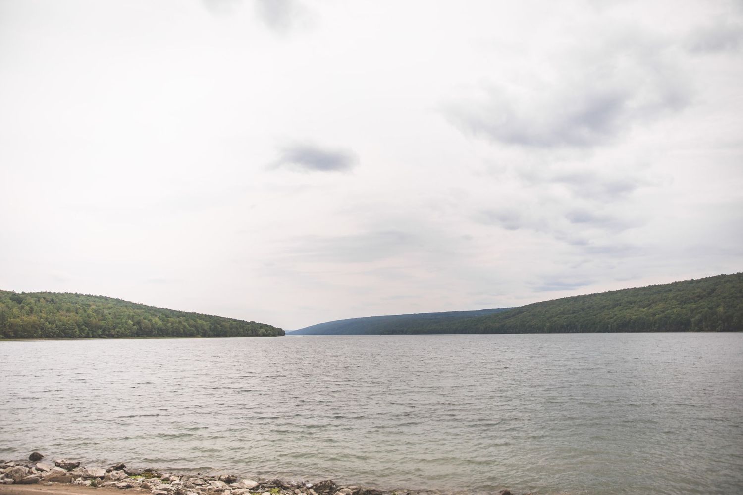 Scenic lakeside landscape with rolling hills and cloudy skies.