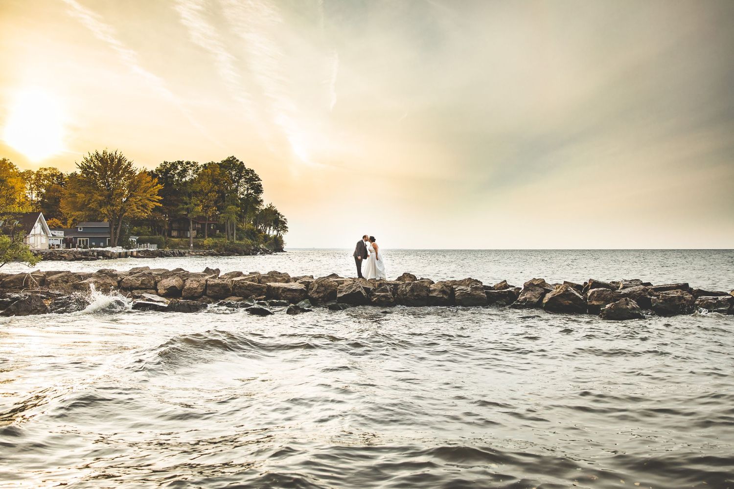 Silhouetted couple on rocky shoreline during sunset with ocean waves.