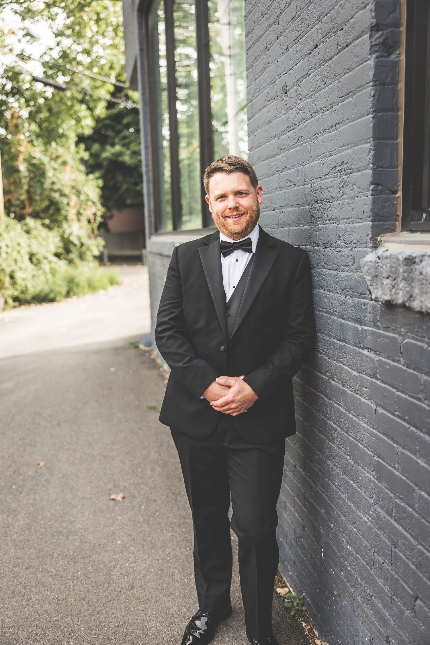 Formal wedding portrait against grey brick wall with natural lighting.