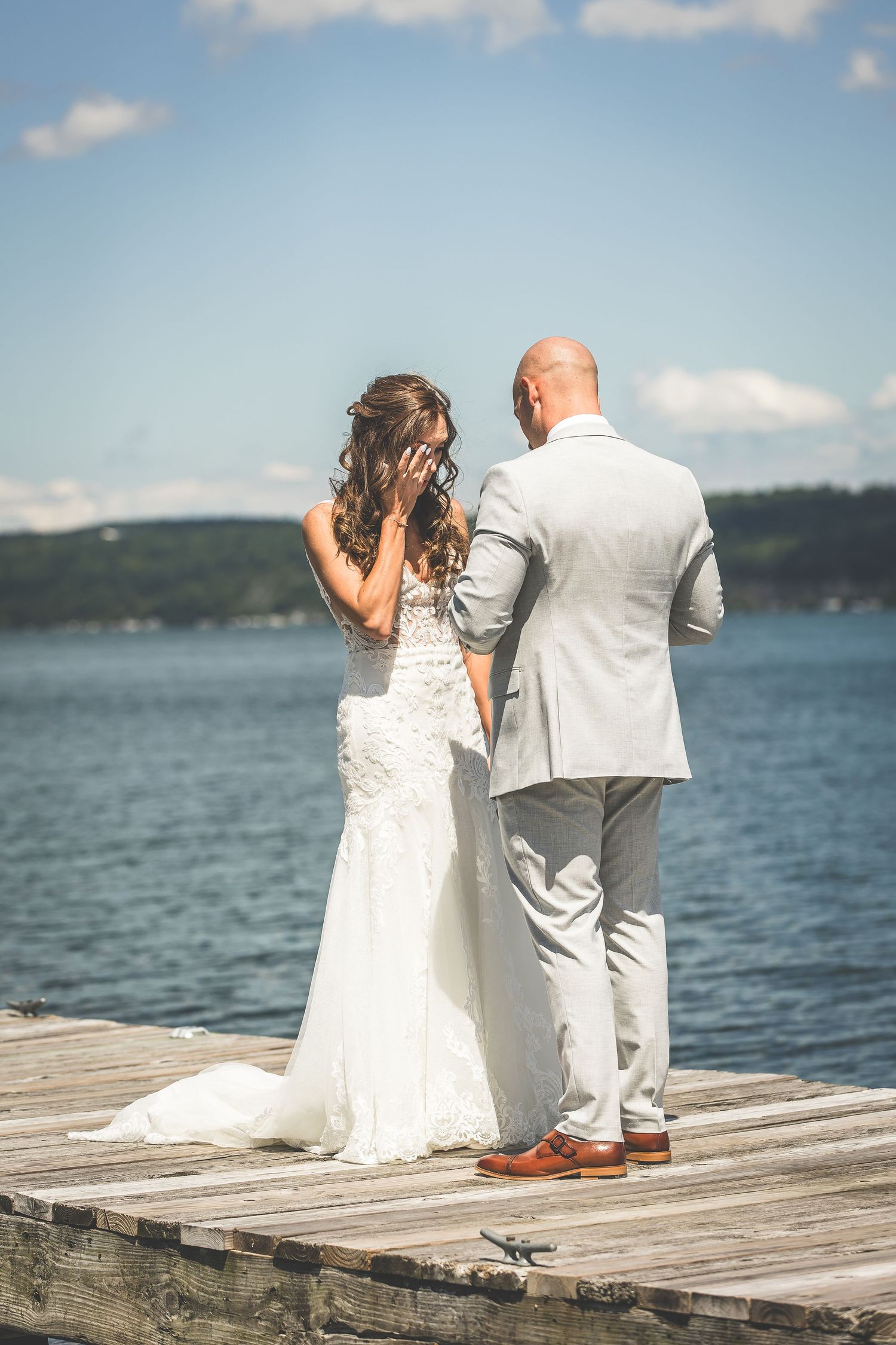 A romantic wedding moment captured from behind as the couple stands on a lakeside pier.