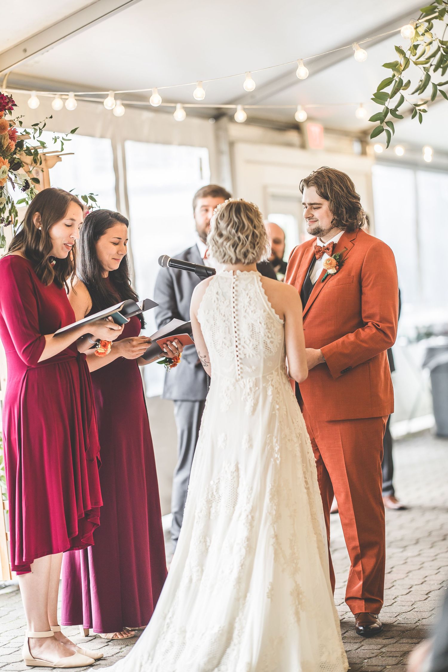 Wedding ceremony participants stand together in burgundy dresses and rust-colored suits.