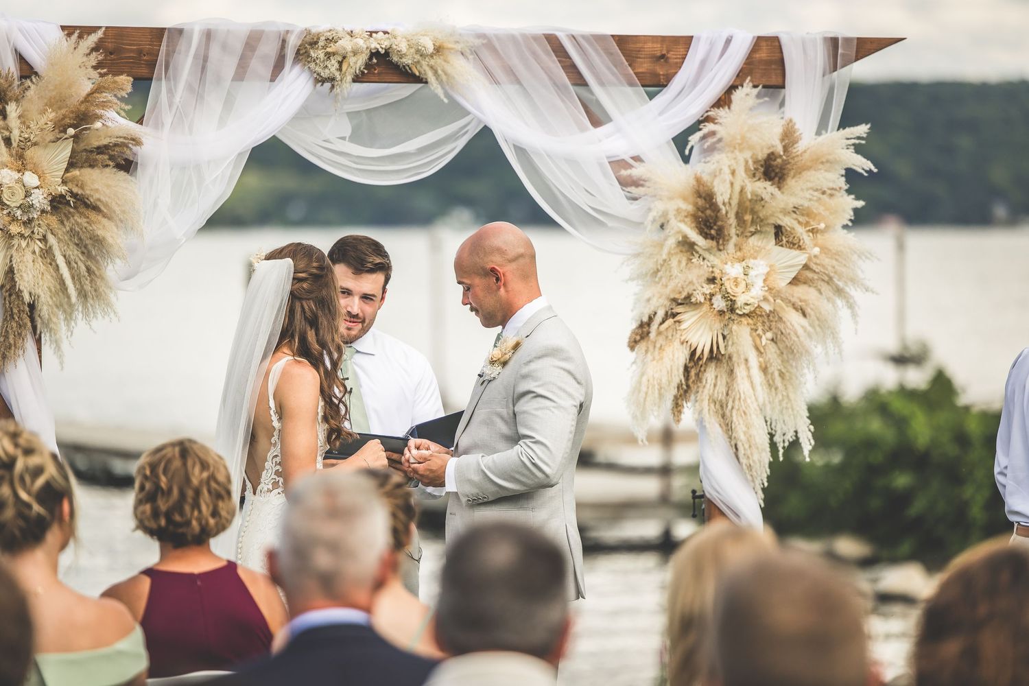 Wedding ceremony moment captured with dried pampas grass decor and waterfront setting.