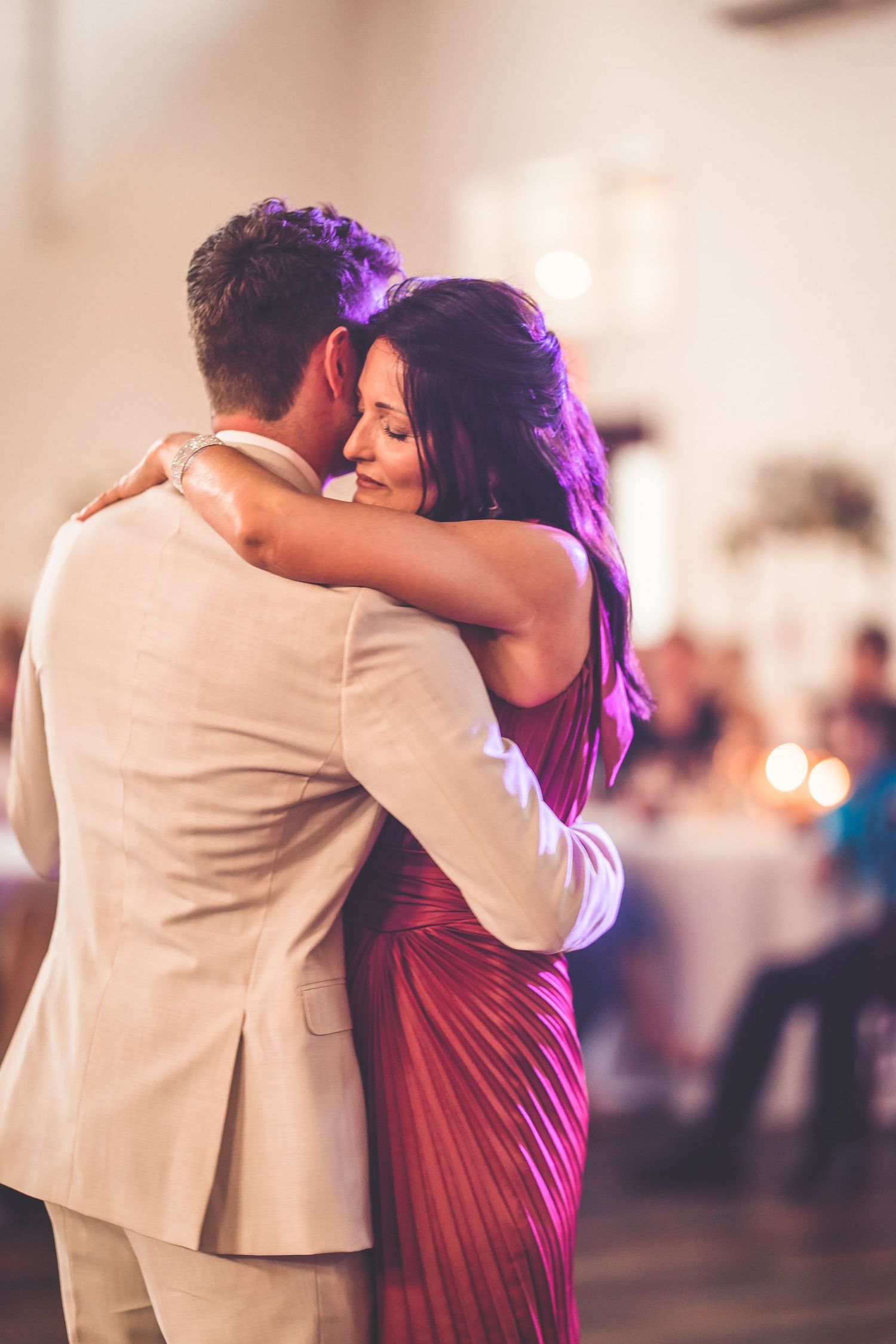 A romantic slow dance moment between two people at an indoor reception with purple lighting.