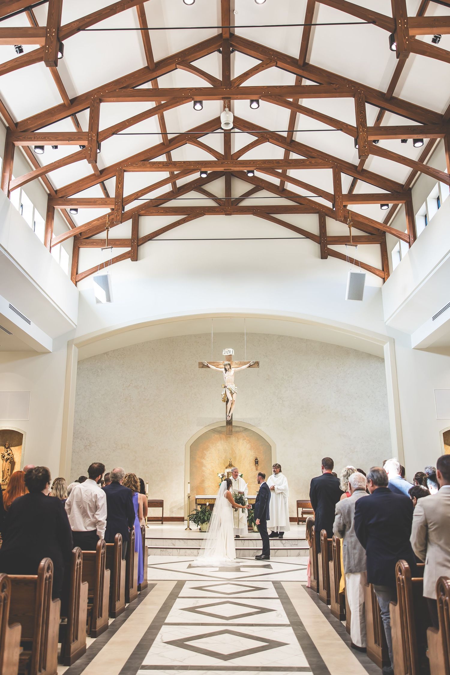 Wide angle view of a church interior with exposed wooden trusses and geometric floor patterns.