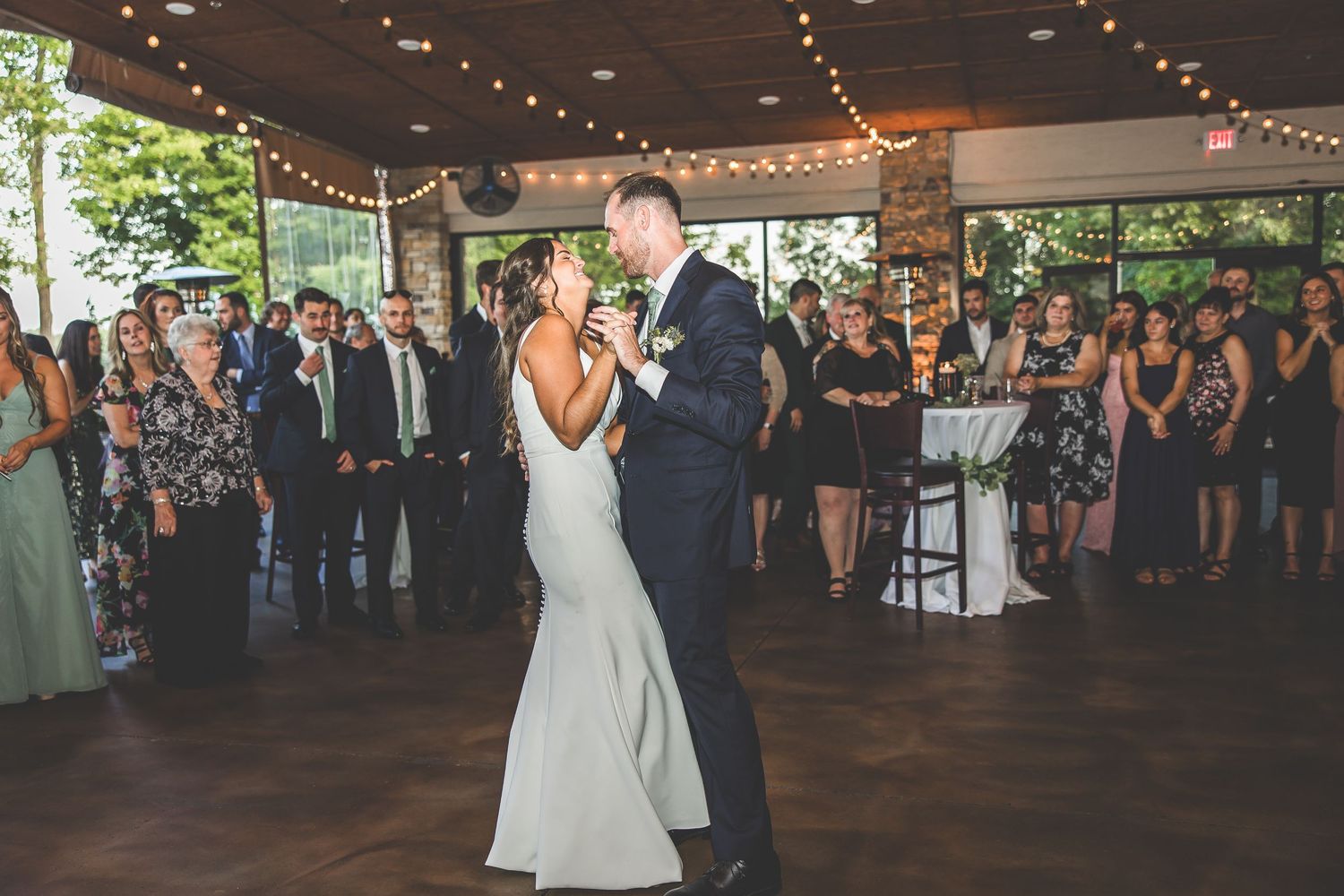 Wedding couple sharing their first dance surrounded by guests at reception venue.