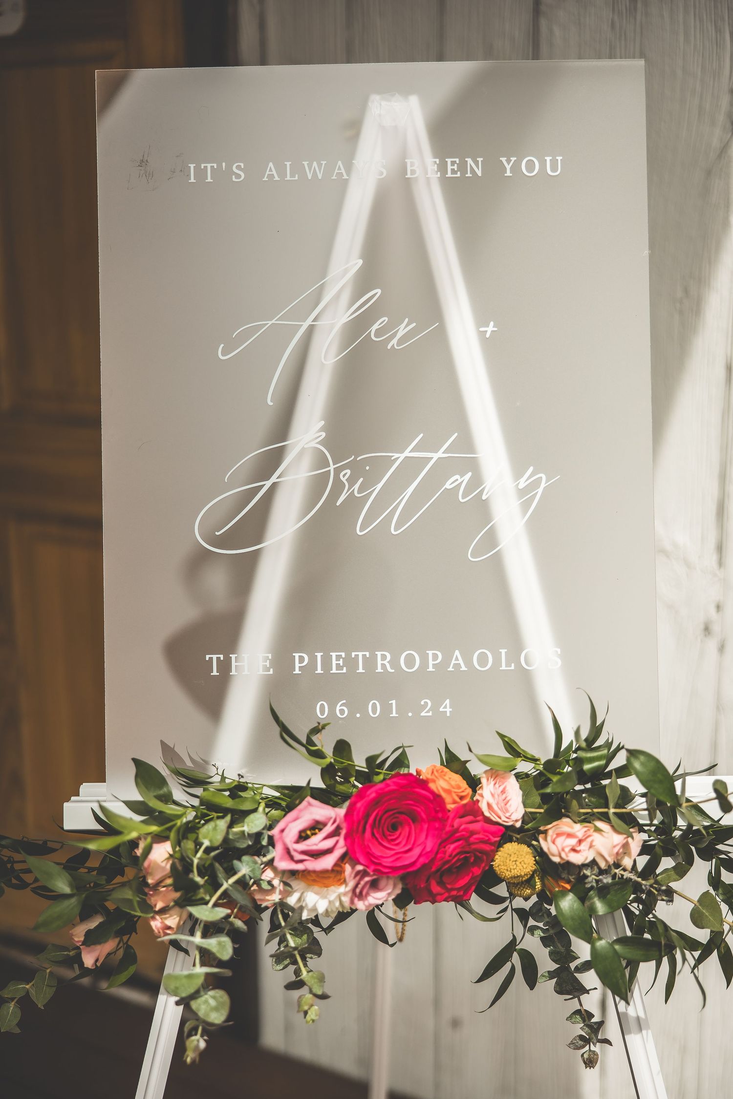 Elegant wedding signage with floral decorations and calligraphy displaying the couple's name and date.