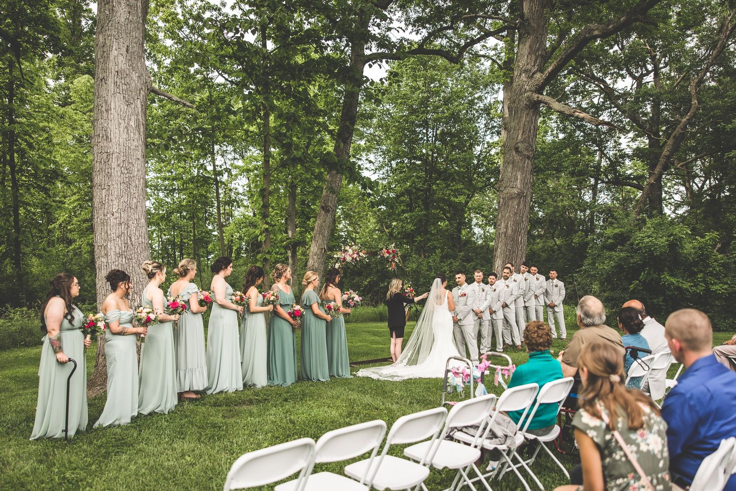 Wedding ceremony setup with bridesmaids in mint dresses and groomsmen in gray suits.