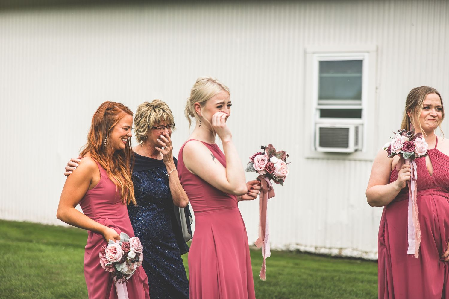 Bridesmaids in coral dresses share a candid moment during outdoor wedding celebration.