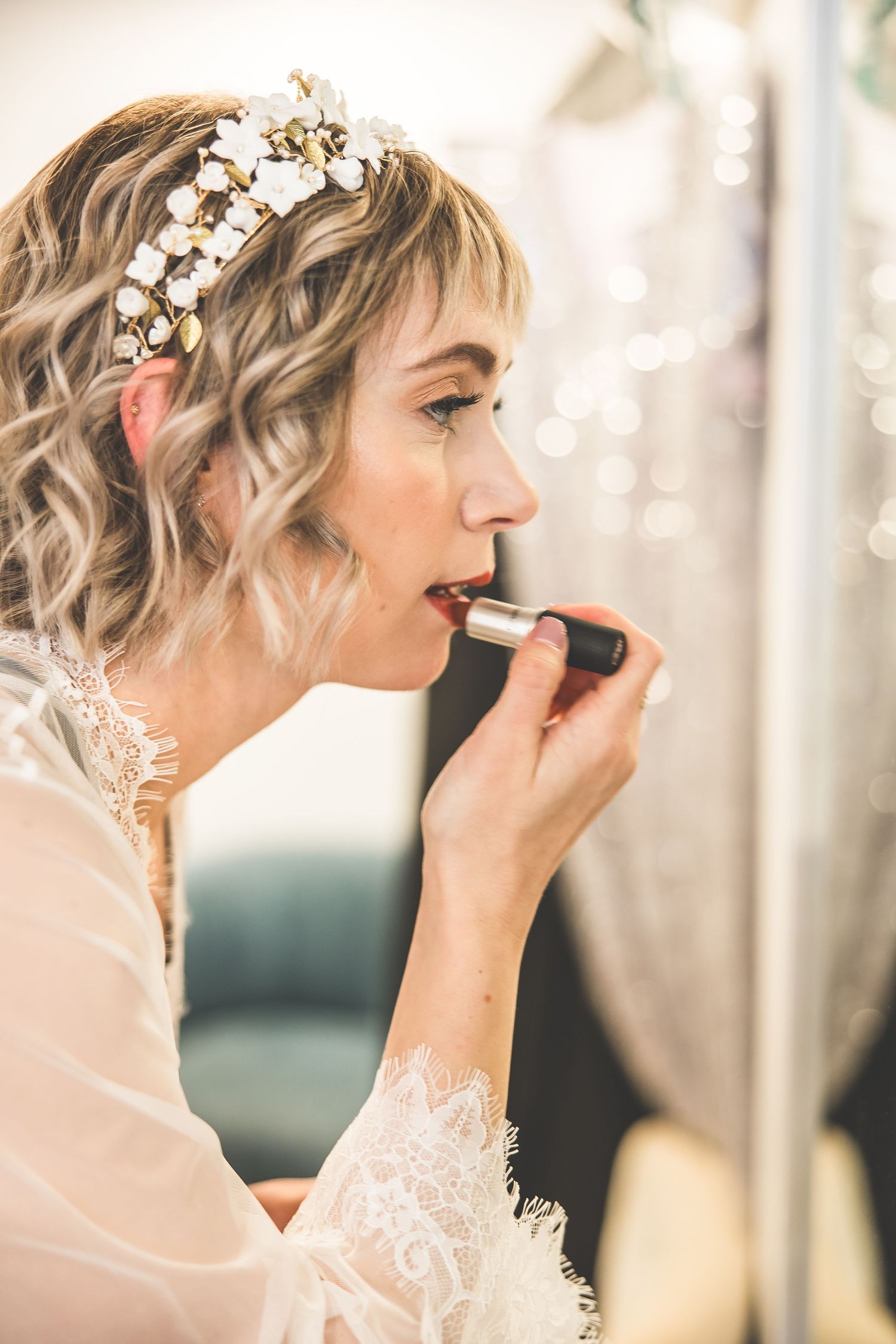 Bride having makeup applied in soft natural light with delicate floral hair accessories.
