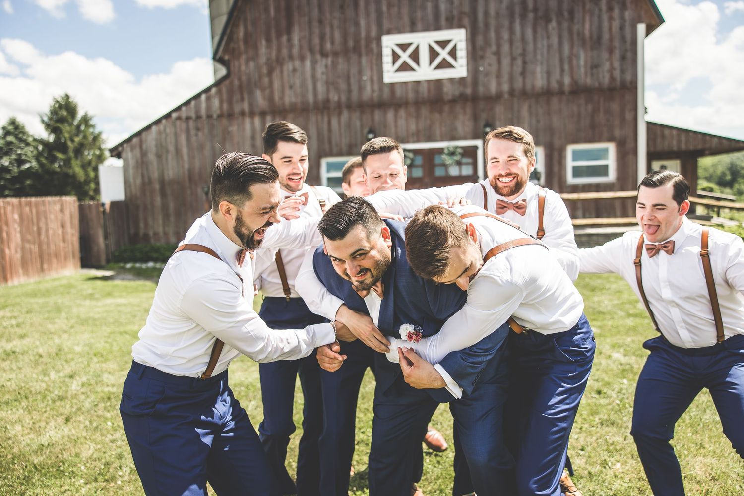Groomsmen in navy pants and white shirts striking fun poses outside barn.