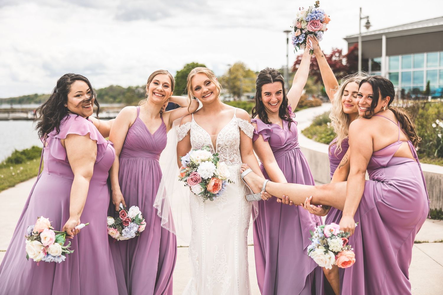 Bridesmaids in flowing mauve dresses celebrating with bride holding floral bouquets.