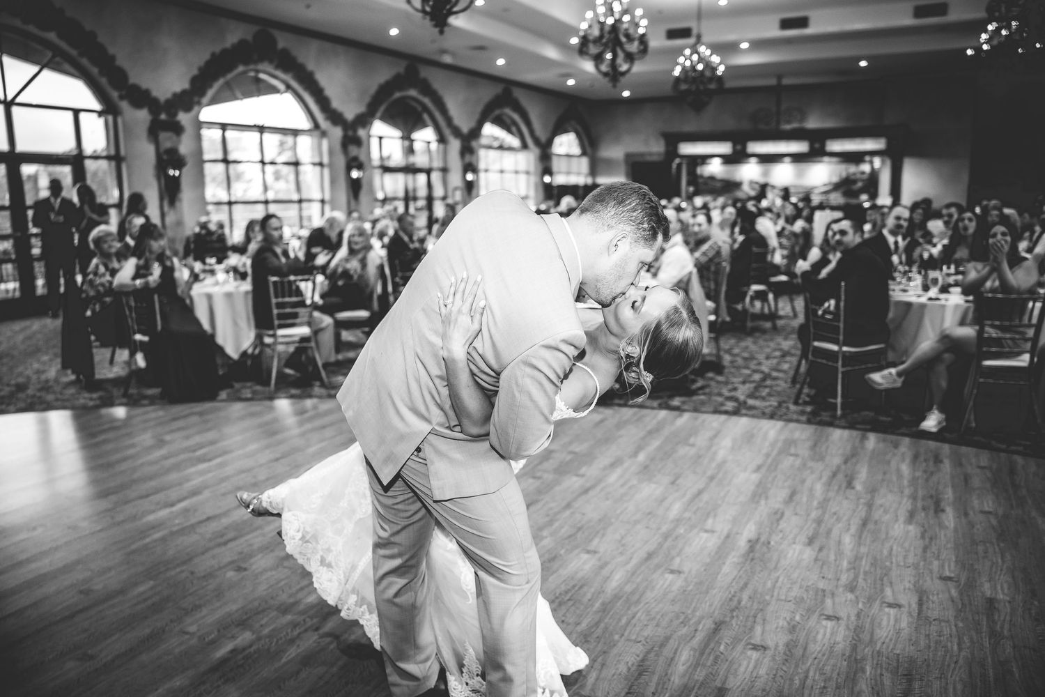 Black and white photo of a couple dancing during their wedding reception in a grand ballroom.