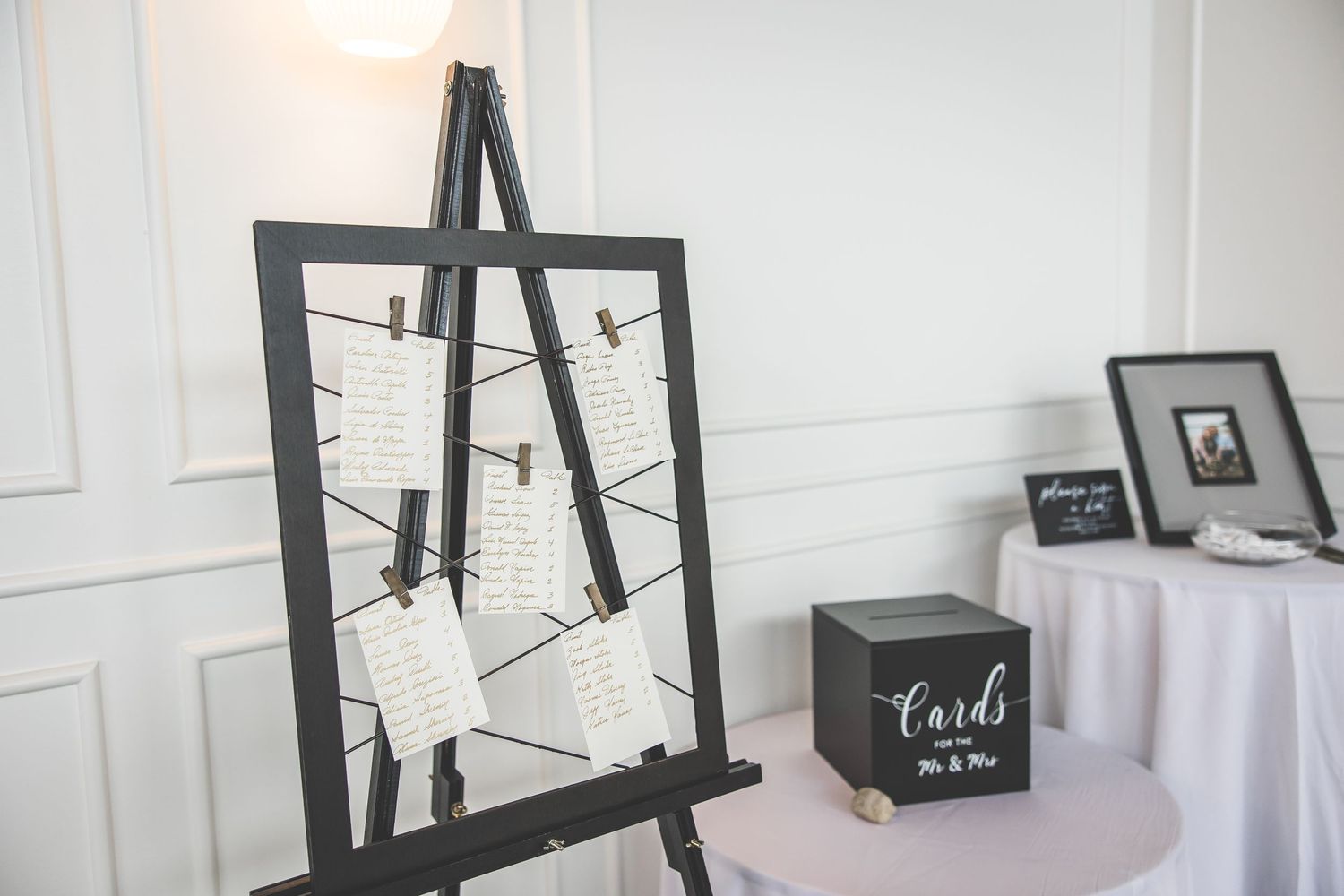 Modern black easel stands displaying wedding signage against a white wall.