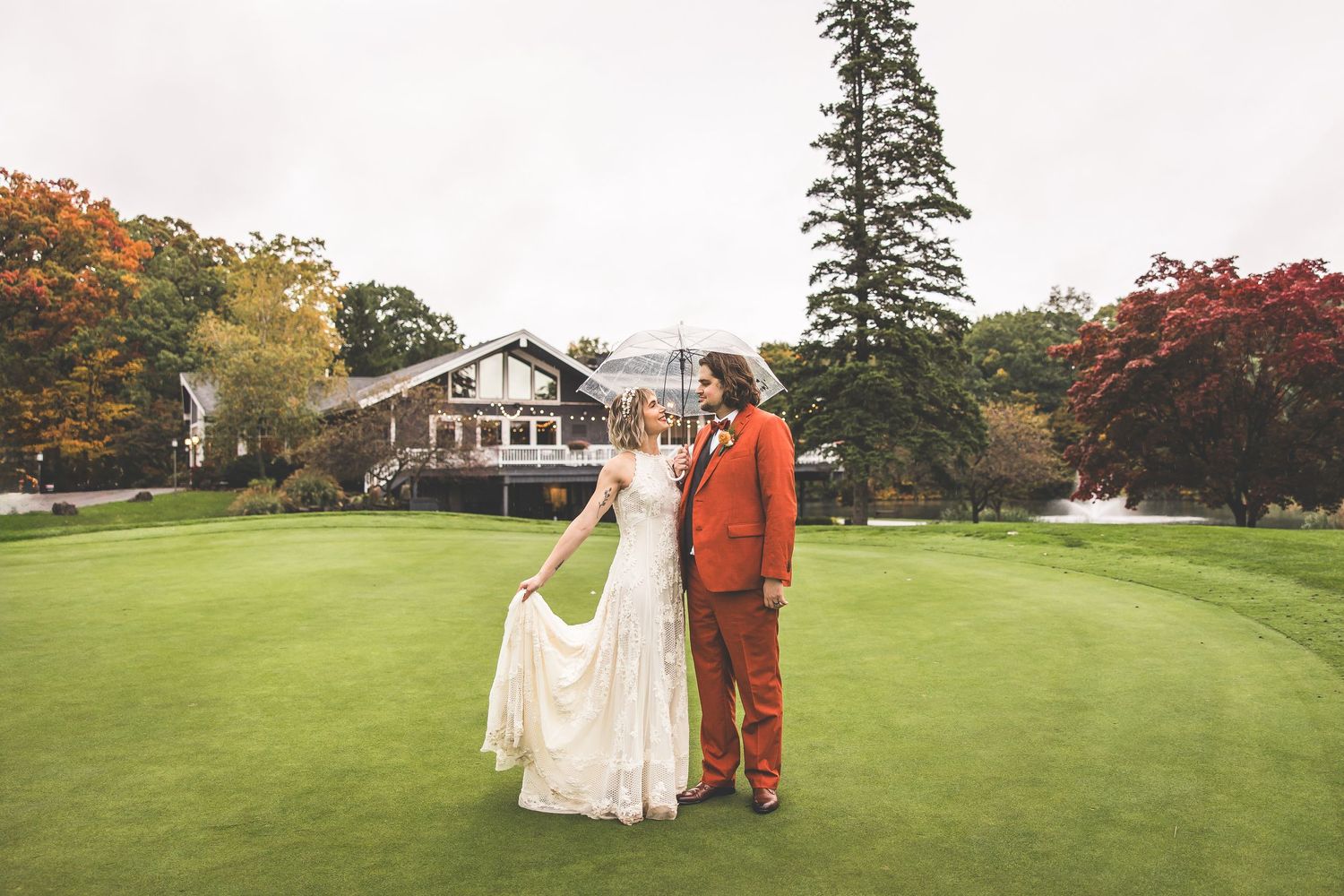 Wedding couple poses on manicured lawn with classic house in background.