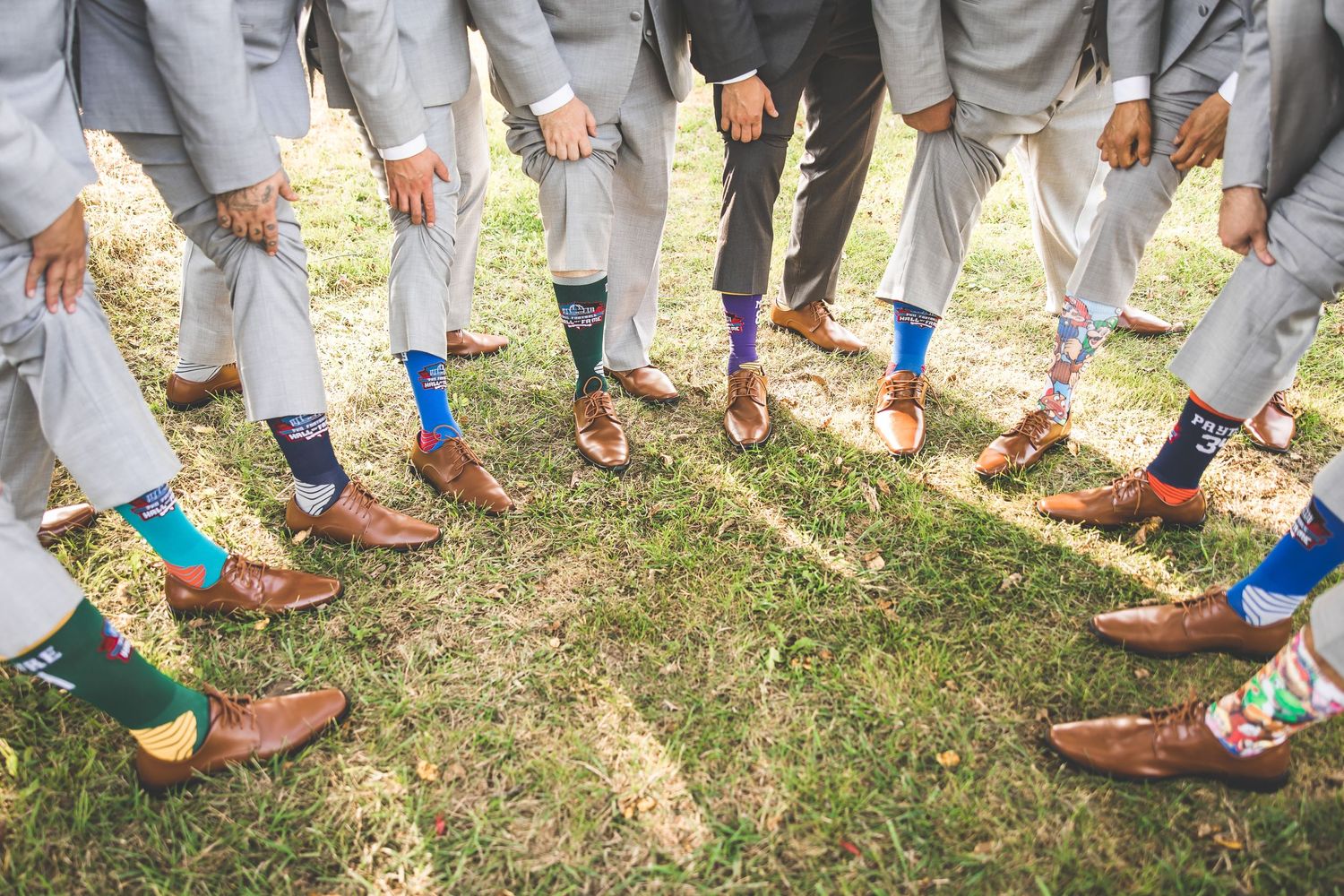 Groomsmen show off colorful socks in circle formation wearing matching gray suits.