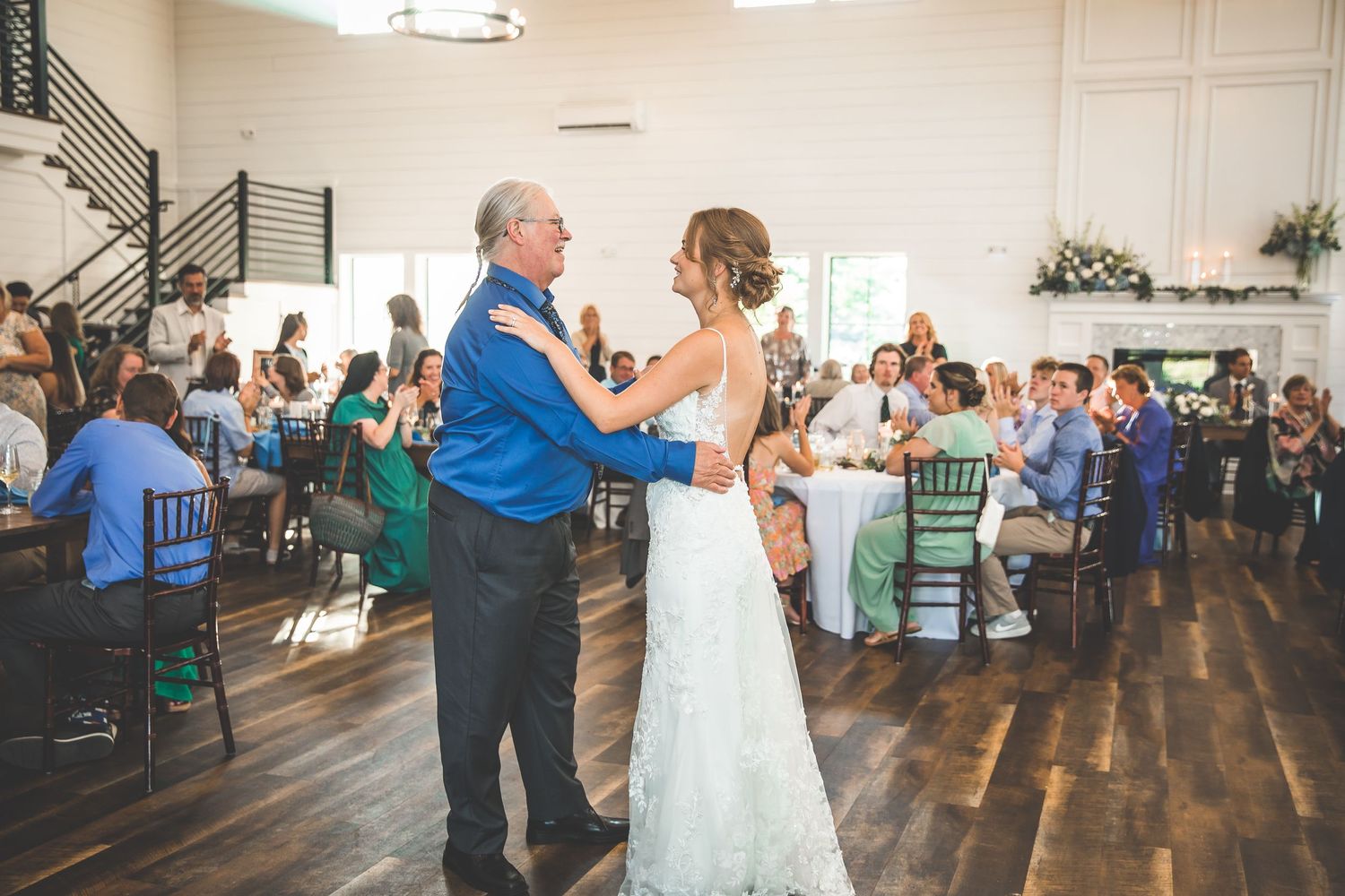 Wedding guests dancing and celebrating in a spacious reception venue with hardwood floors.