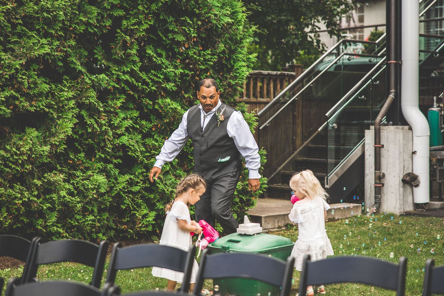 Wedding party members celebrate outdoors near a wooden staircase surrounded by greenery.