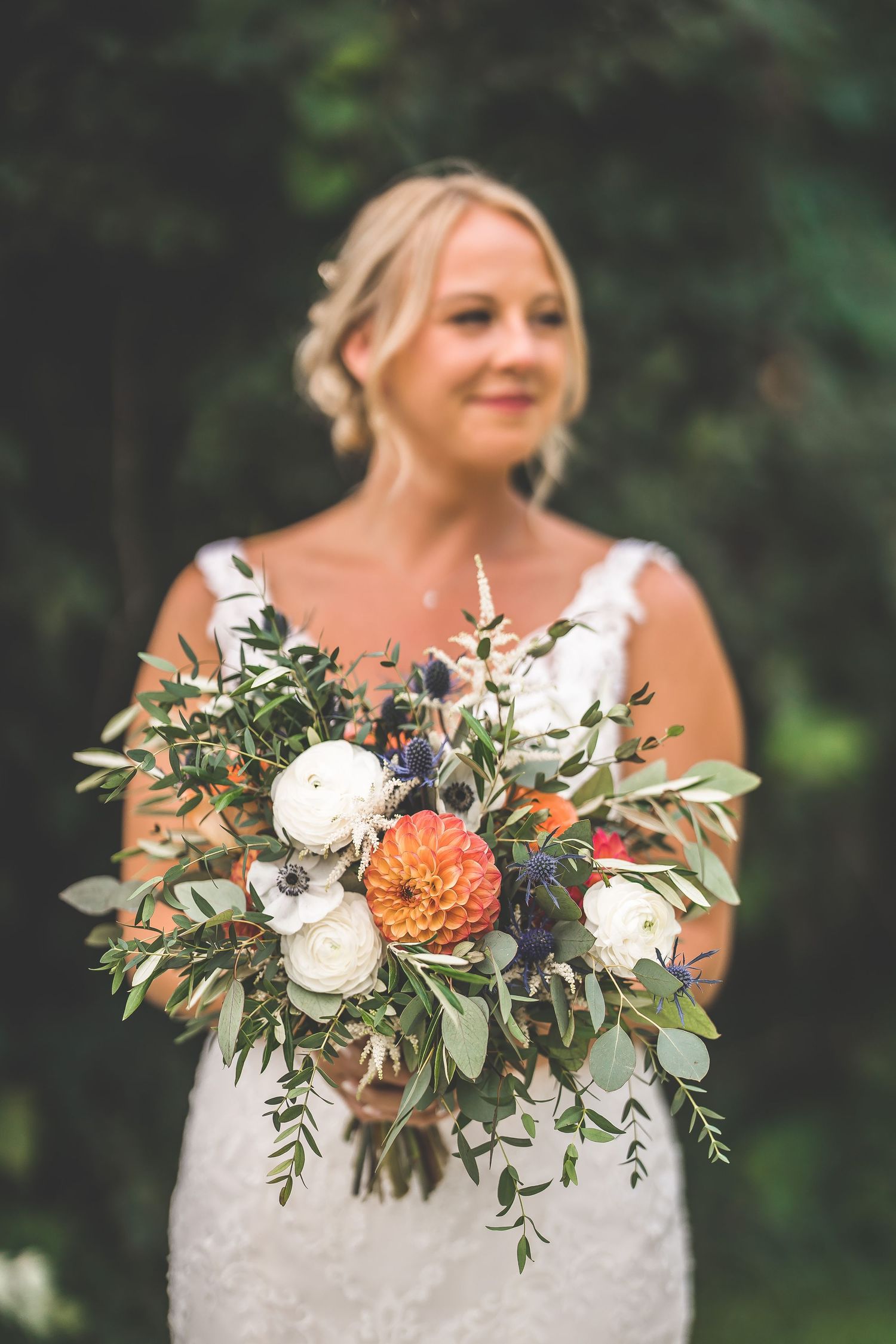 Beautiful bridal bouquet featuring coral dahlias, white roses and greenery against wedding dress.