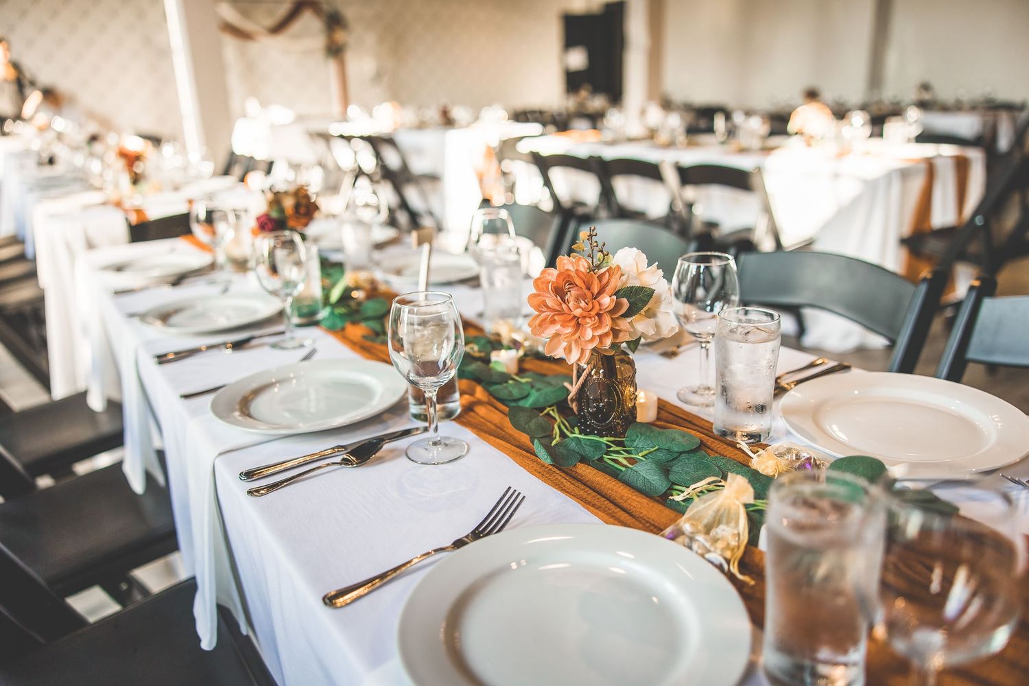 An elegant wedding reception table setting with white linens and orange floral centerpieces.