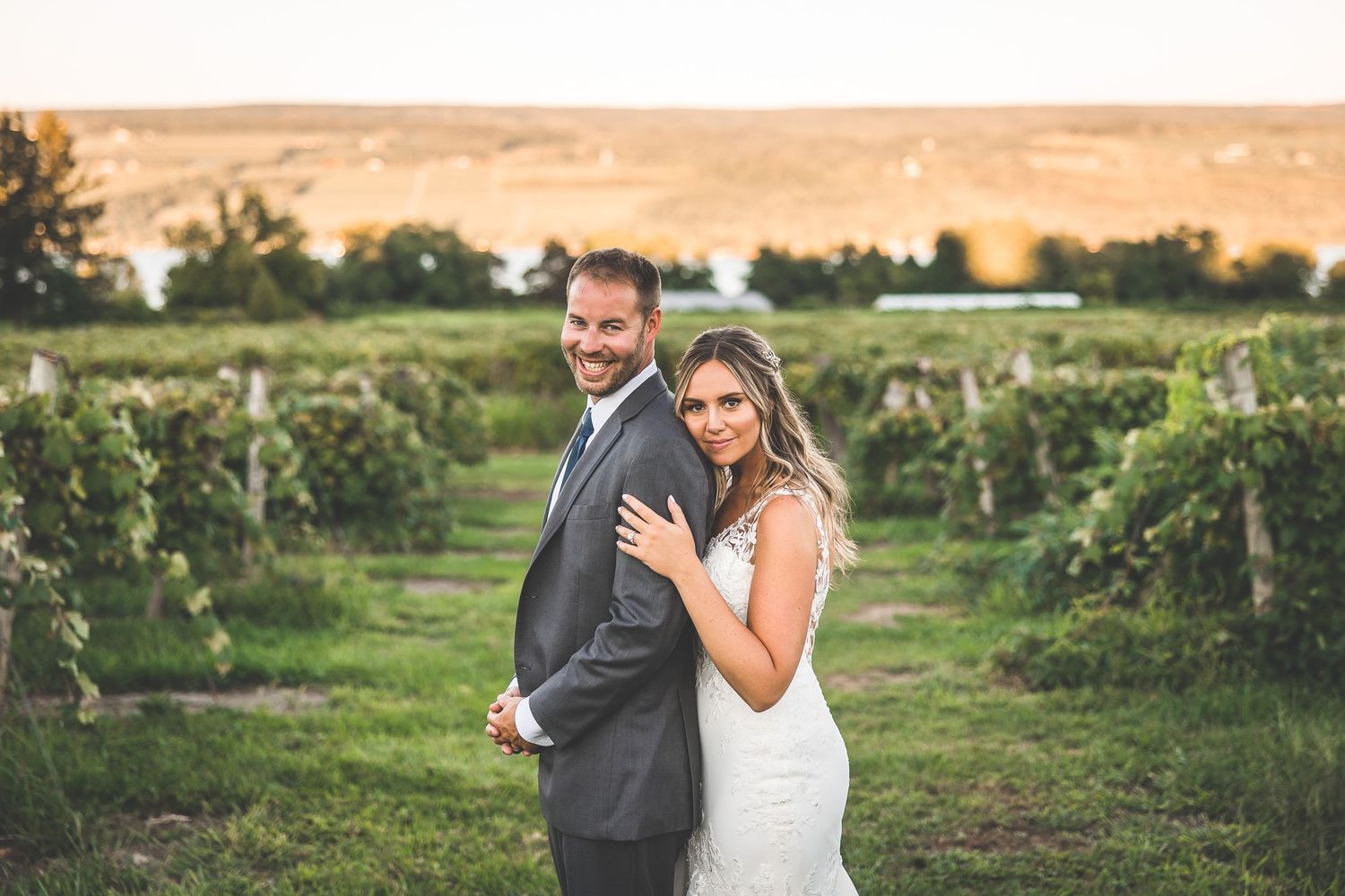 Wide landscape shot of vineyard with newlyweds embracing among the grape vines.