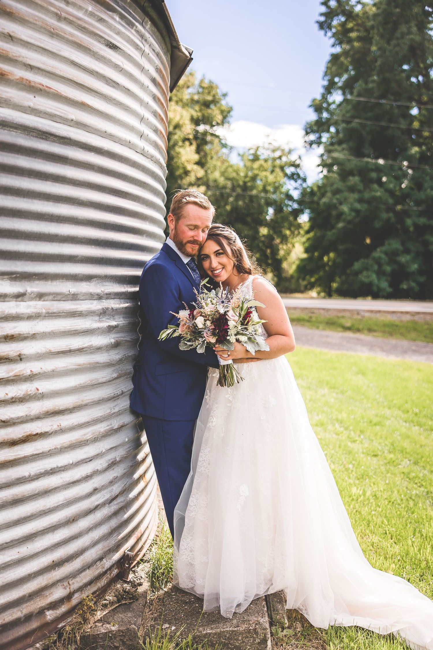 Rustic wedding photos featuring a couple posing near a corrugated metal silo in a grassy field.