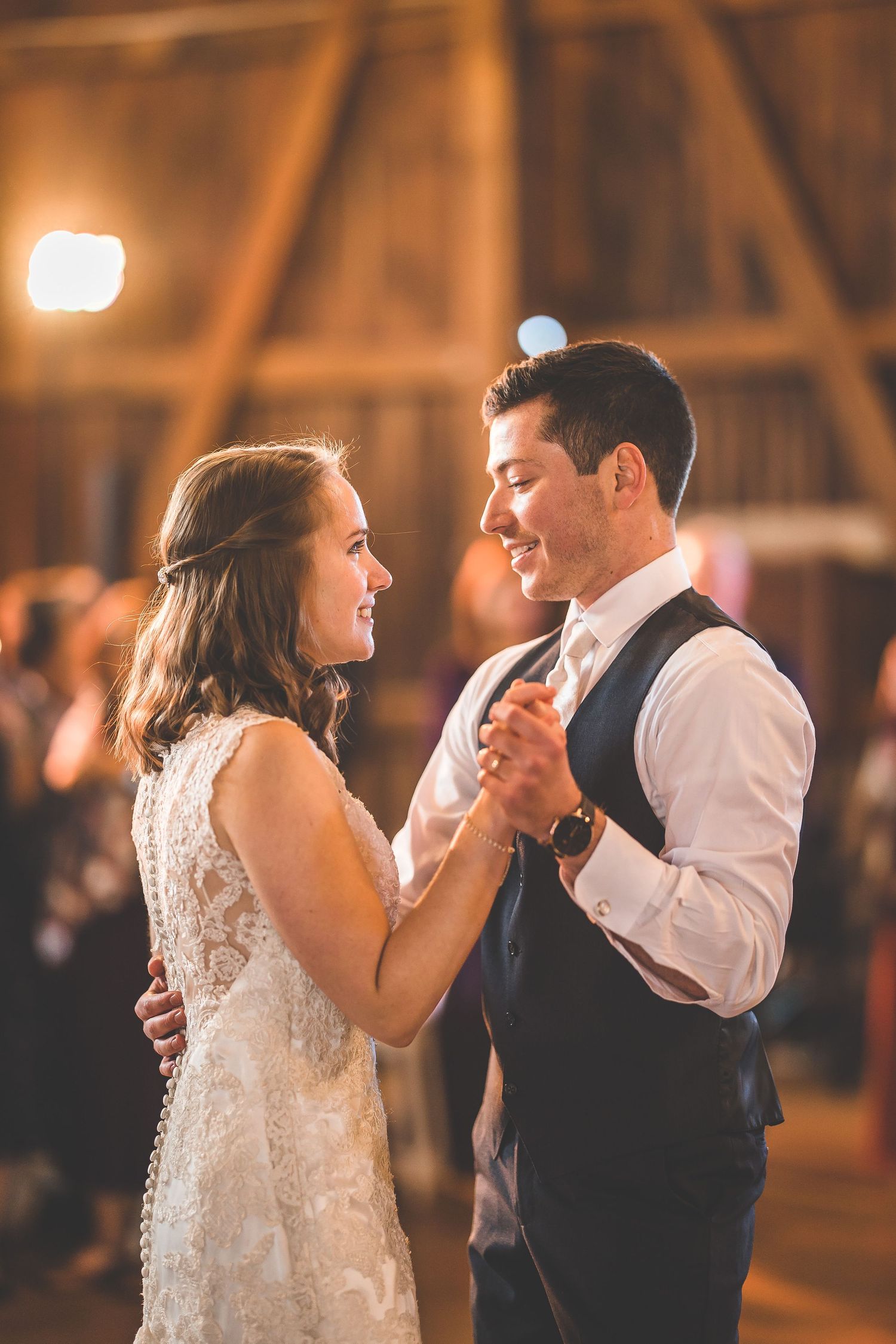 Newlyweds share their first dance in a warmly lit rustic barn venue.