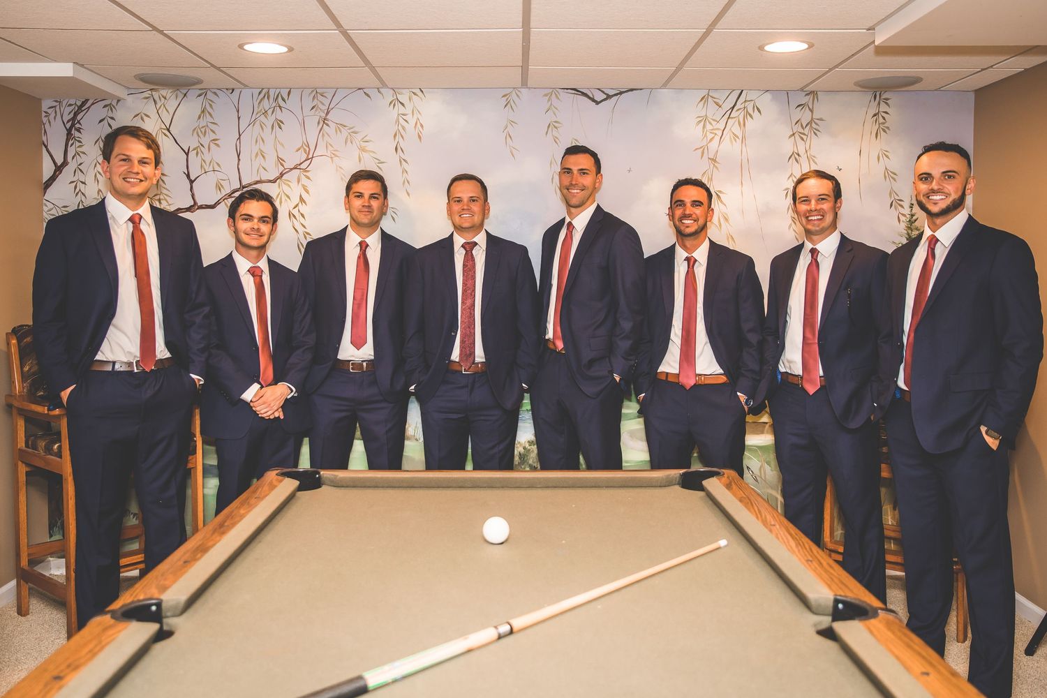 Groomsmen playing pool and socializing in formal attire at a wedding venue.